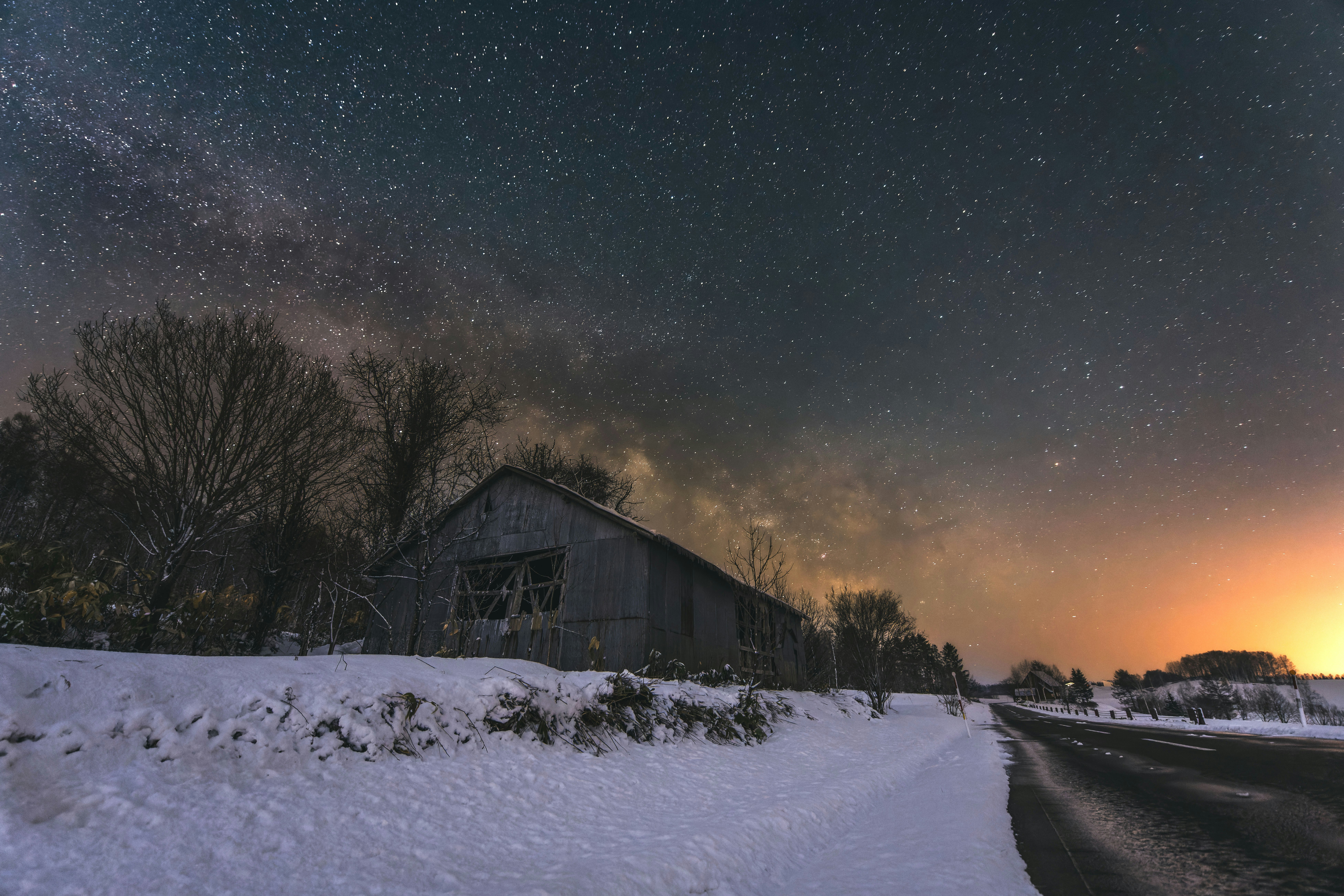 Milky Way rising over an abandoned house along a snowy field