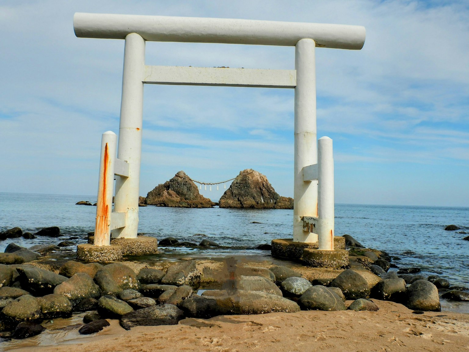 Gerbang torii putih dengan pemandangan laut dua batu di latar belakang