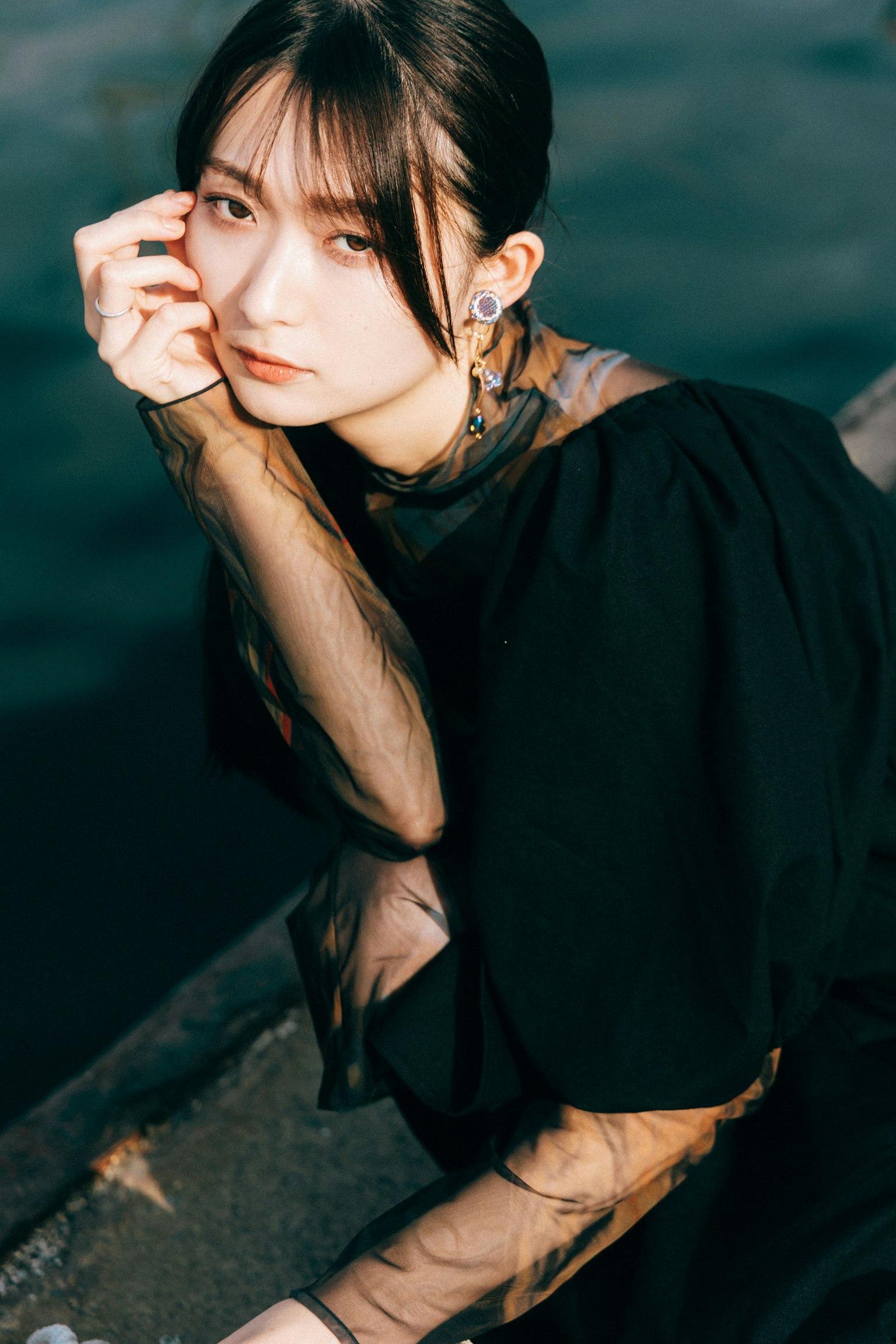 一位穿著黑色服裝的女性坐在水邊，表情沉思