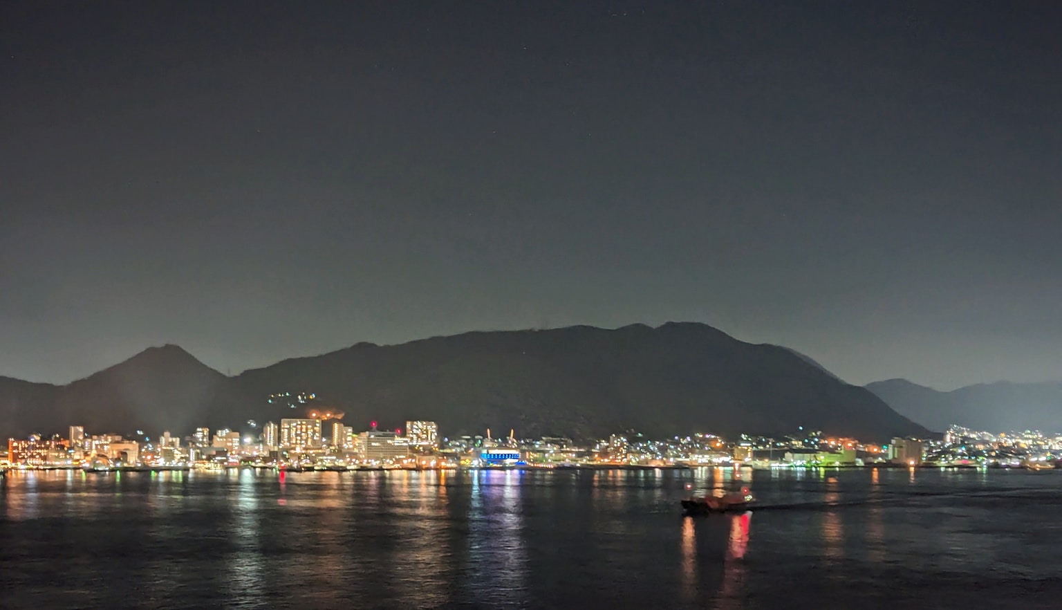 City lights reflecting on the water at night with a mountain backdrop