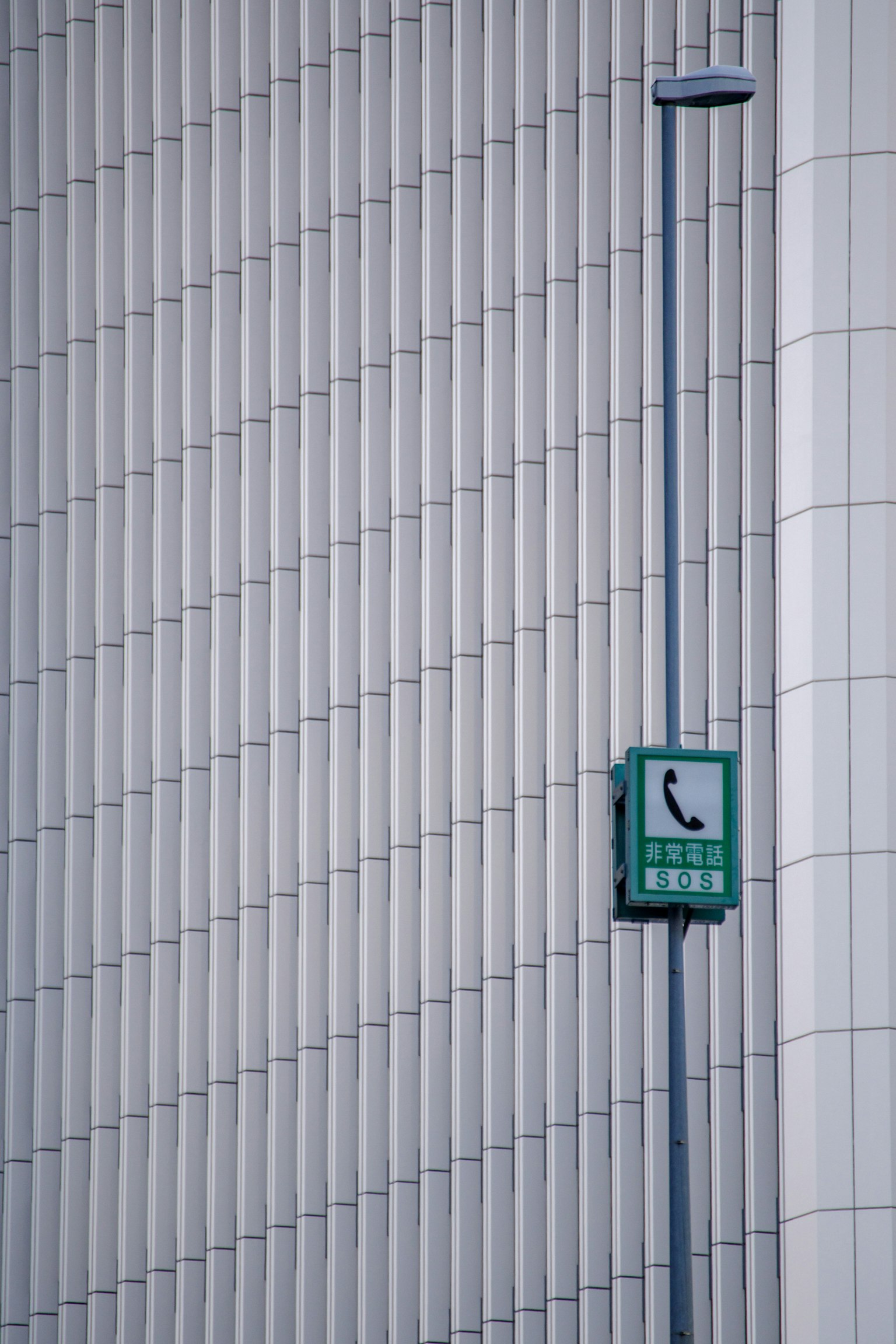 Green public phone box attached to a white vertical striped wall