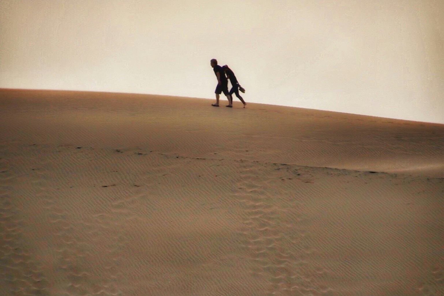 Silhouette einer Person, die auf einer Sanddüne mit Fußabdrücken geht