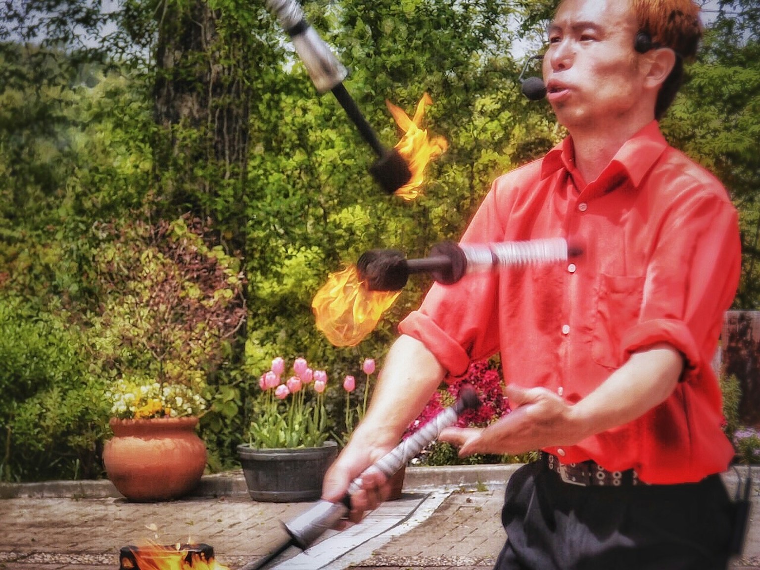 Homme jonglant avec du feu portant une chemise rouge arbres verts en arrière-plan