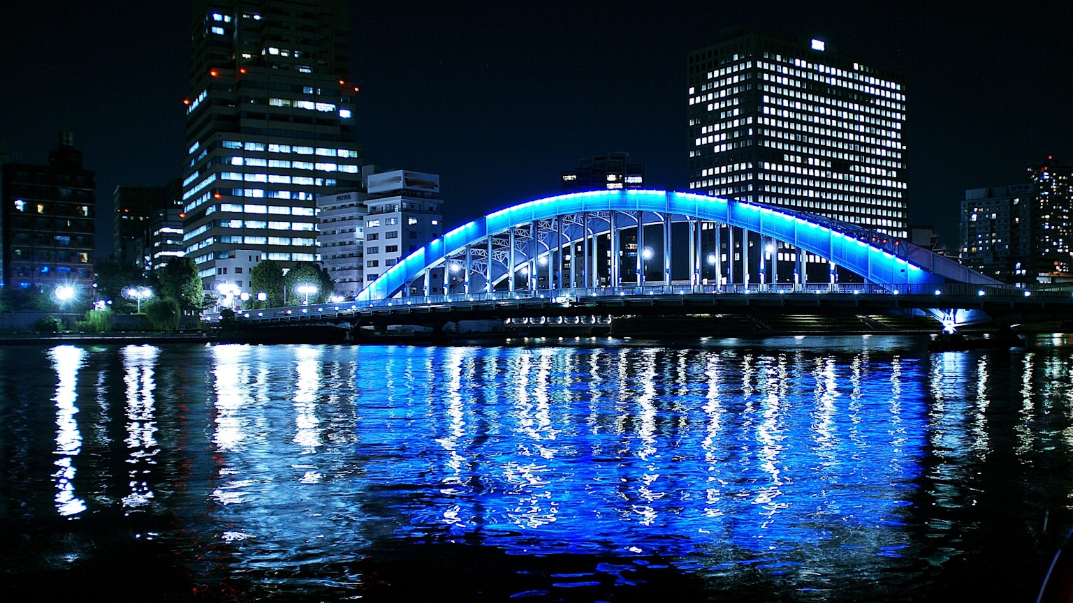 Night cityscape featuring a glowing blue bridge and reflections on the water
