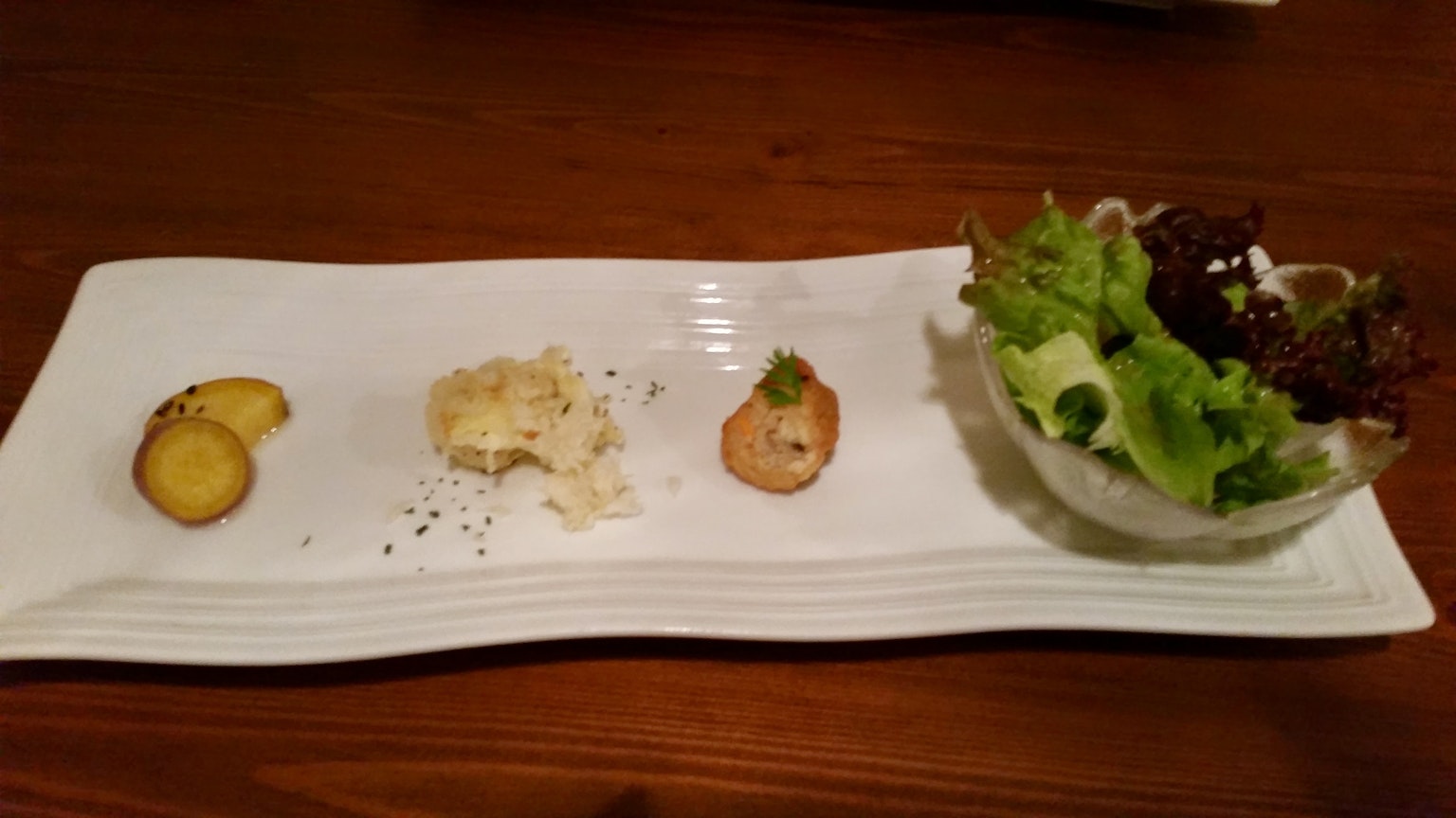 Un vassoio di antipasti su un piatto bianco con insalata, fette di patate e un piatto cremoso
