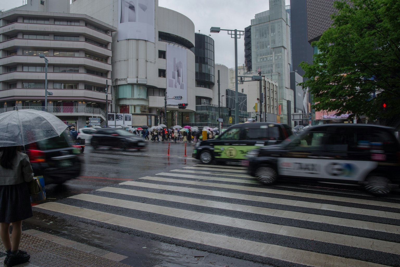 Busy urban crosswalk on a rainy day with pedestrians and cars