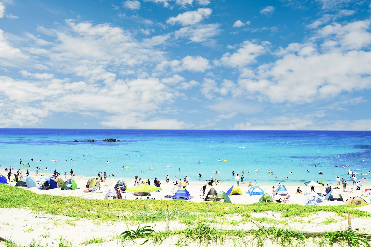 ชายหาดที่มีคนพลุกพล่านเพลิดเพลินกับทะเลและท้องฟ้าสีฟ้า