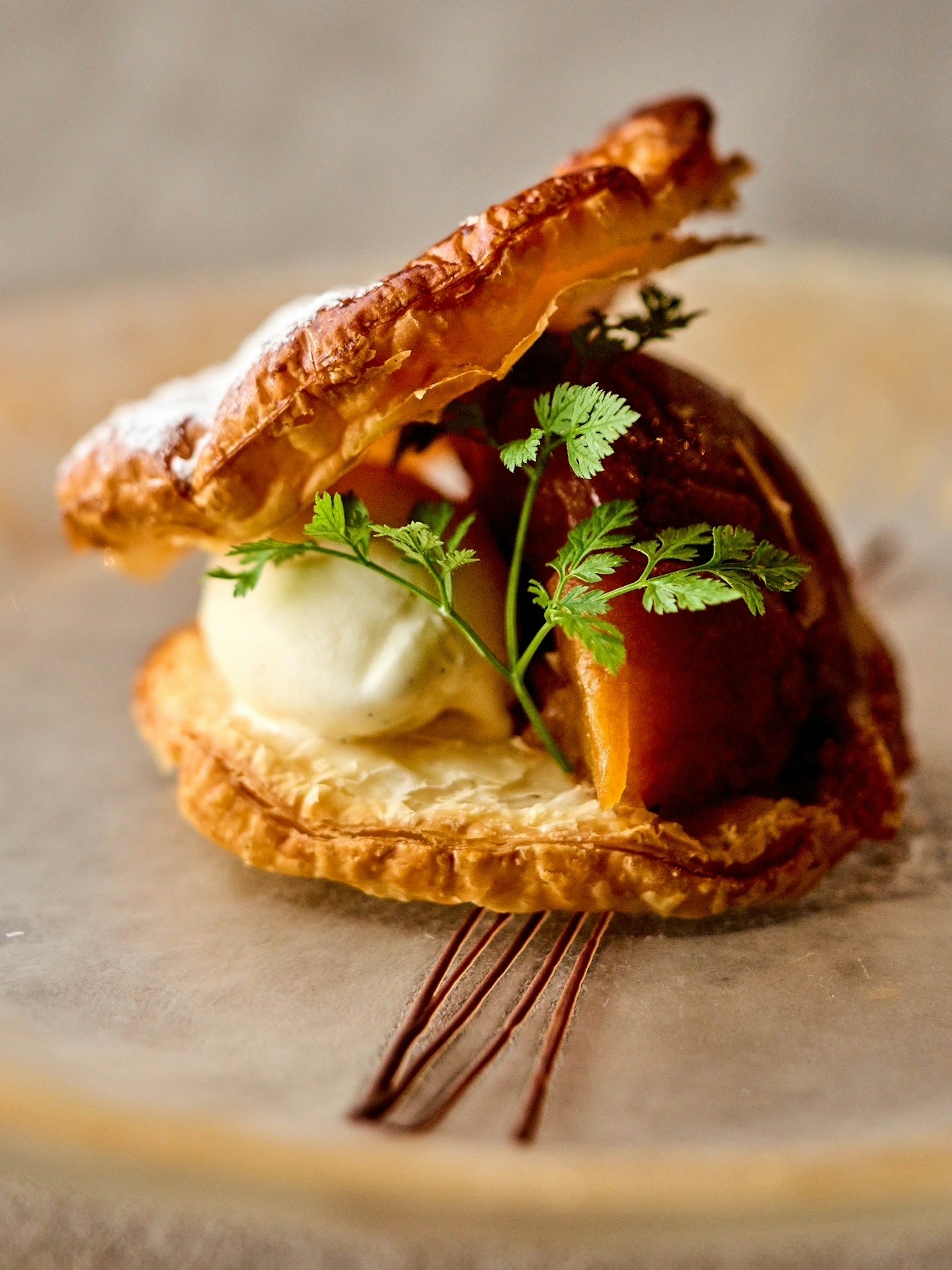 Dessert featuring flaky pastry with ice cream and garnished with fresh herbs