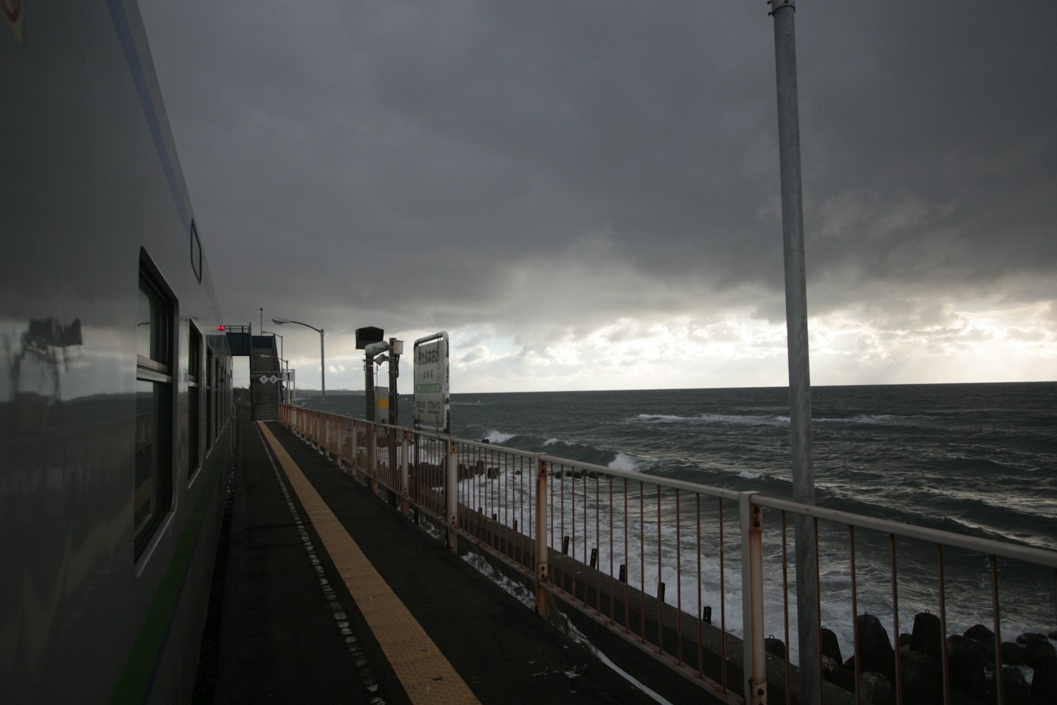 Paisaje marítimo nublado con una plataforma de tren y olas