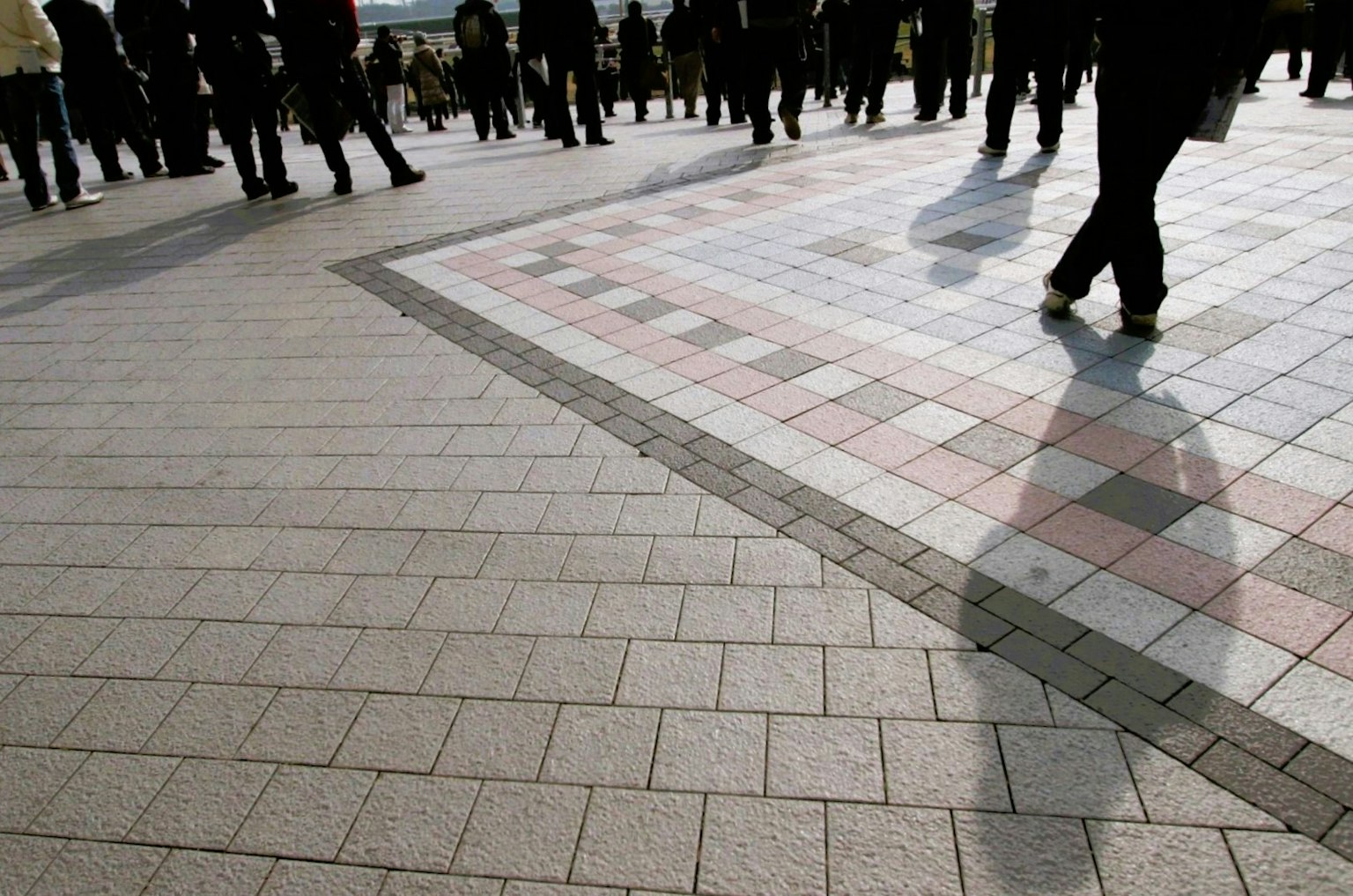 Foule de personnes marchant sur un pavé à motifs avec des ombres