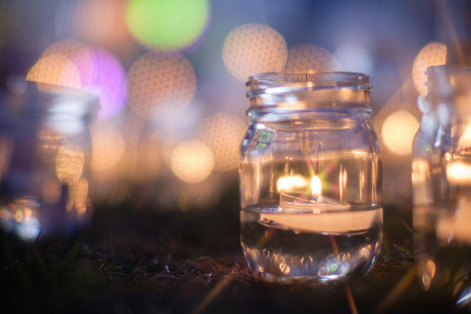 Un bocal en verre avec une bougie posé sur de l'herbe dans un cadre nocturne