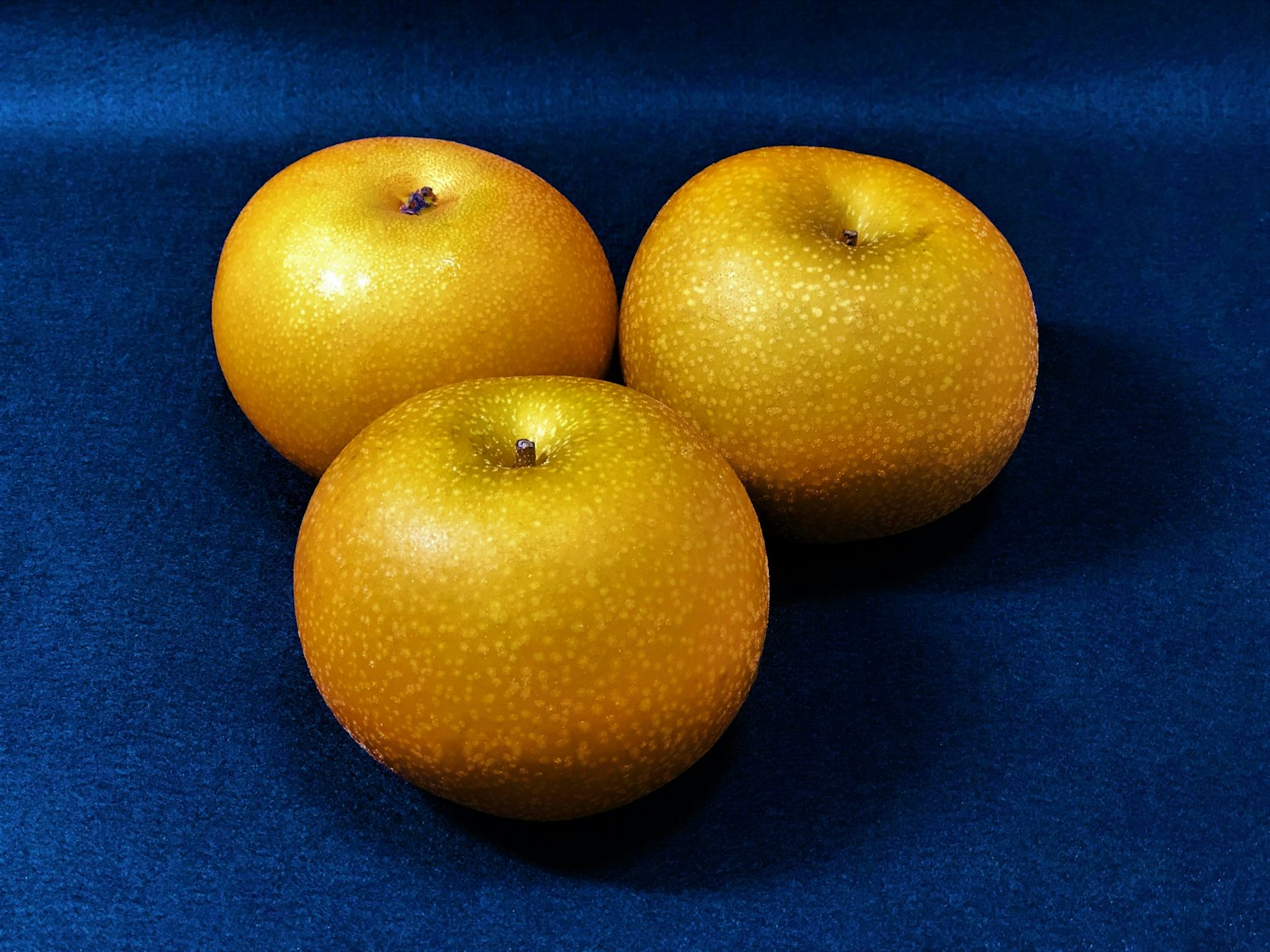 Trois fruits orange placés sur un fond de tissu bleu