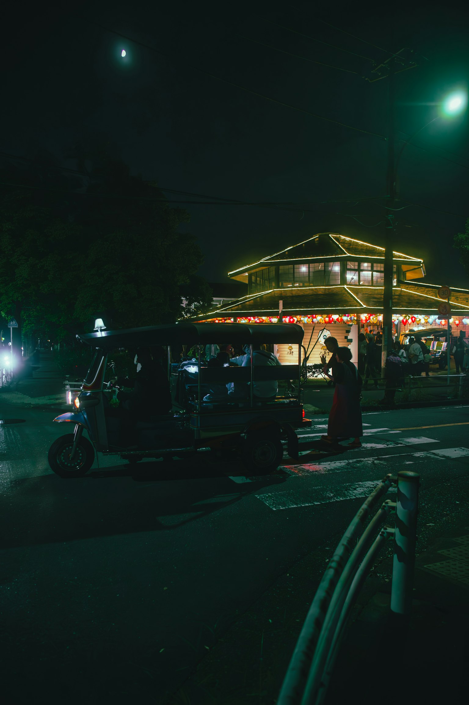 Scena notturna con un tuk-tuk fermo all'angolo di una strada Edificio illuminato e luci dei veicoli visibili