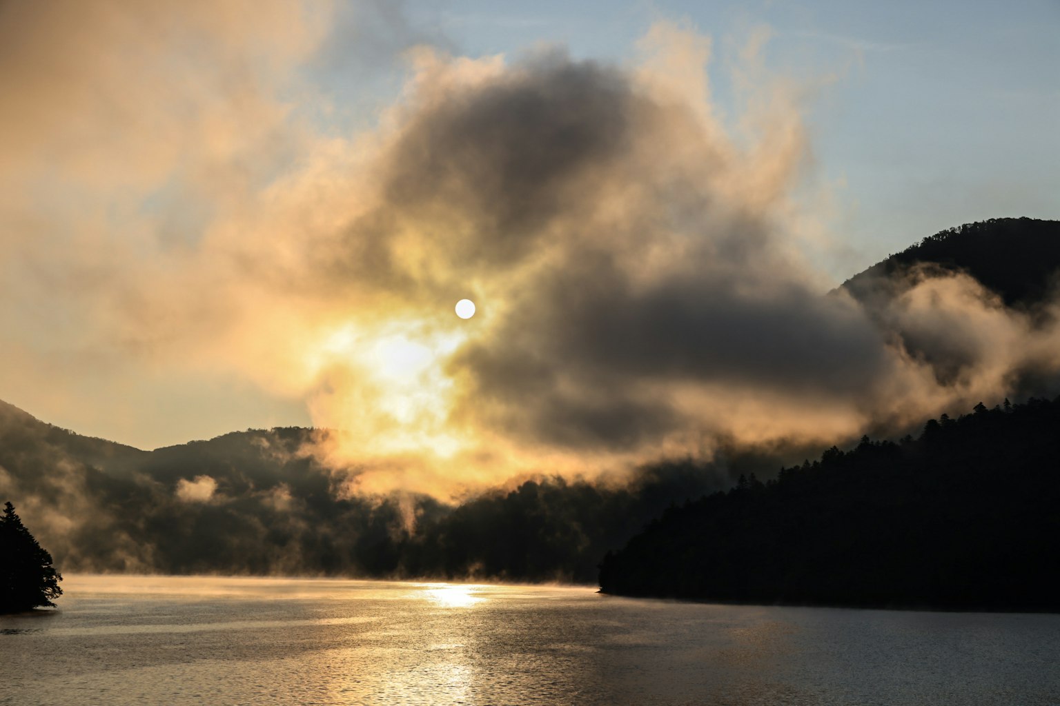 Pemandangan indah danau saat matahari terbenam dengan kabut dan pegunungan