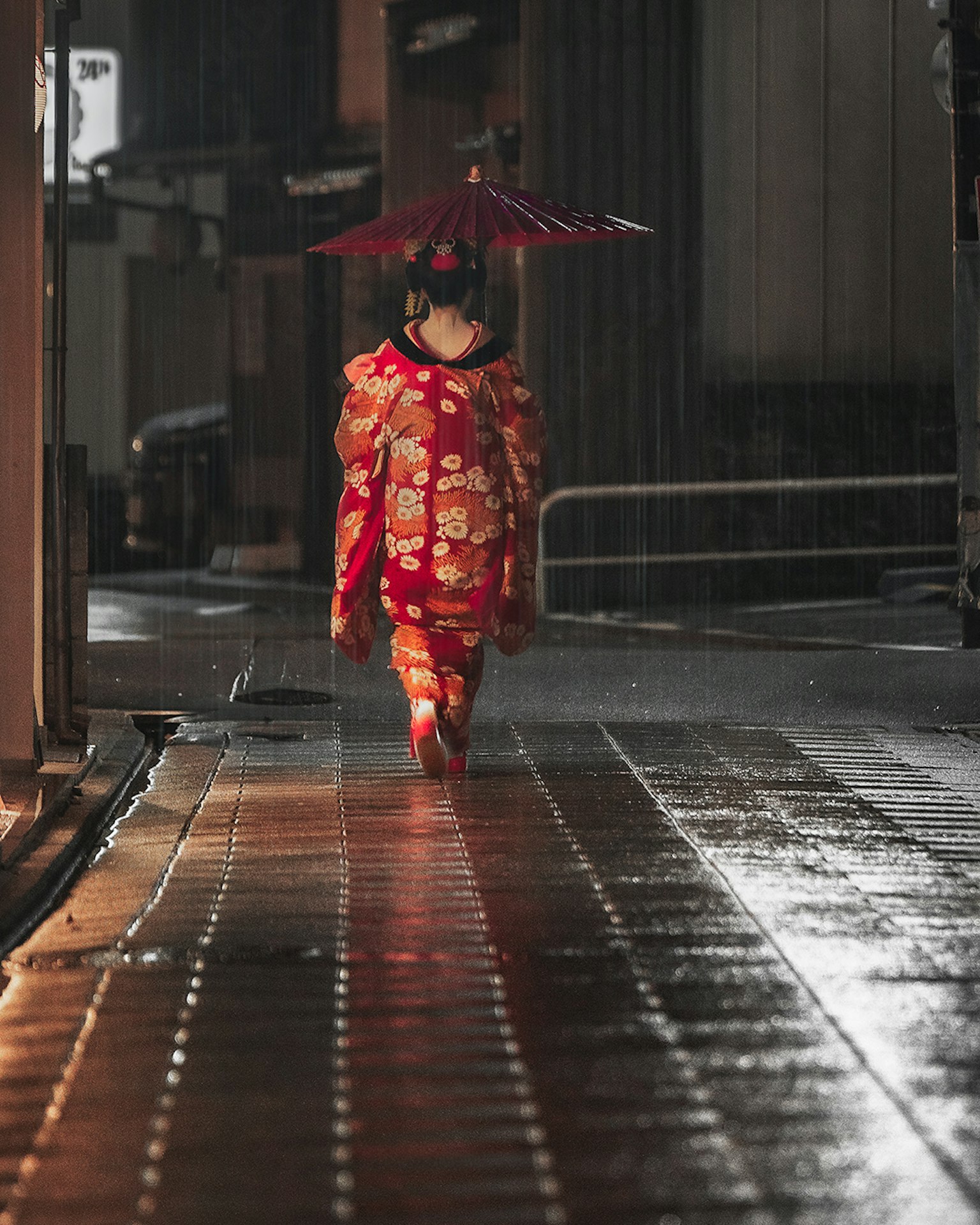 一位穿着红色和服的女性在雨中撑着伞行走