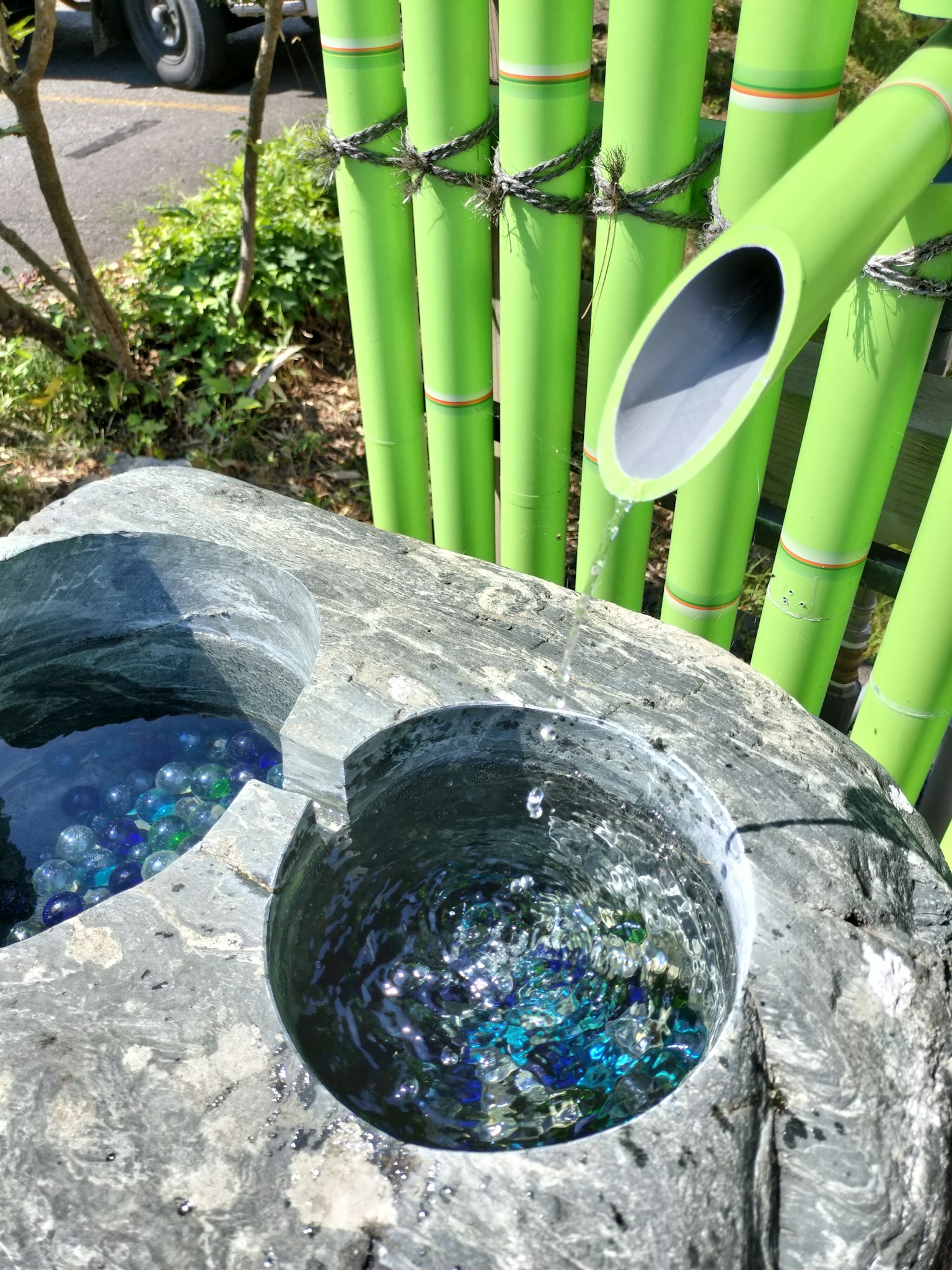 A serene scene featuring green bamboo and a stone water basin with colorful glass marbles inside
