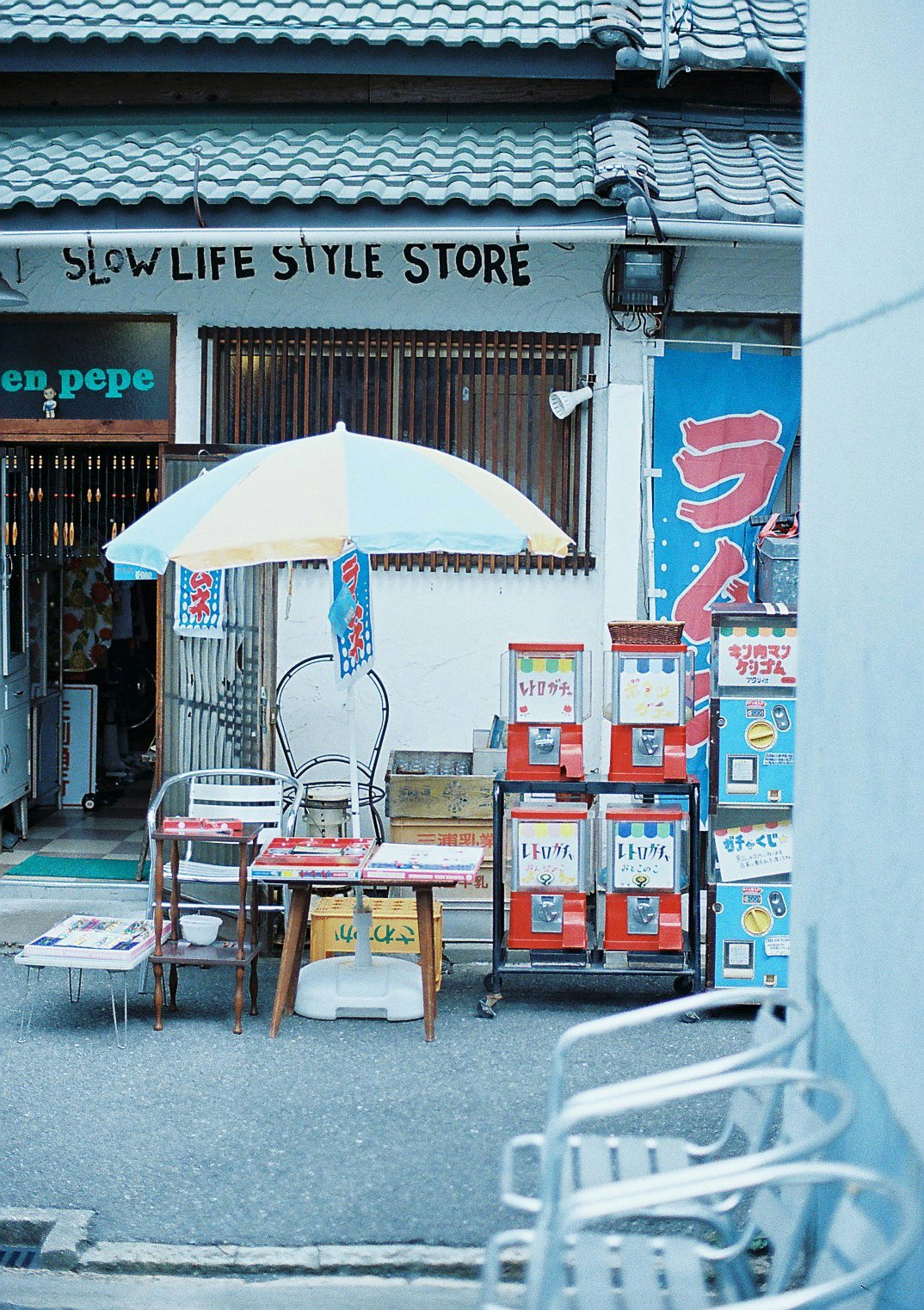 Narrow alley storefront with “SLOW LIFE STYLE STORE” signage, tables and an umbrella