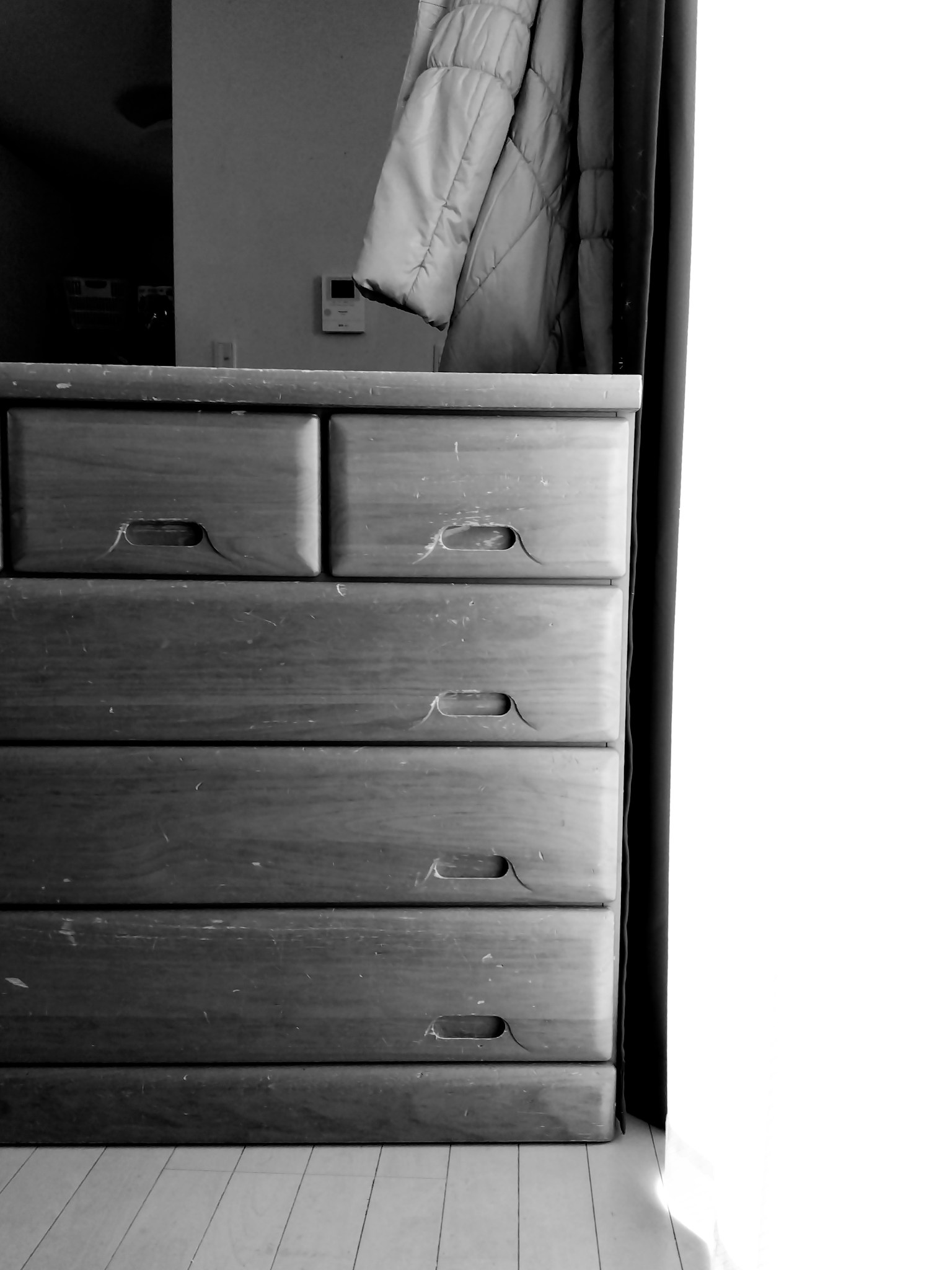 Black and white image of a wooden dresser with drawers and a coat