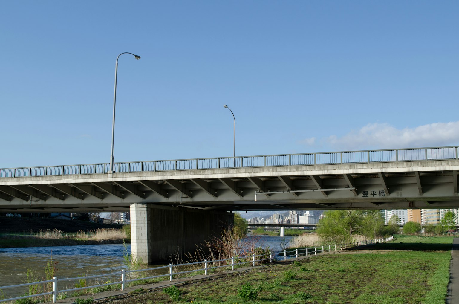 Bridge over a river under a clear blue sky featuring green grass and a white fence