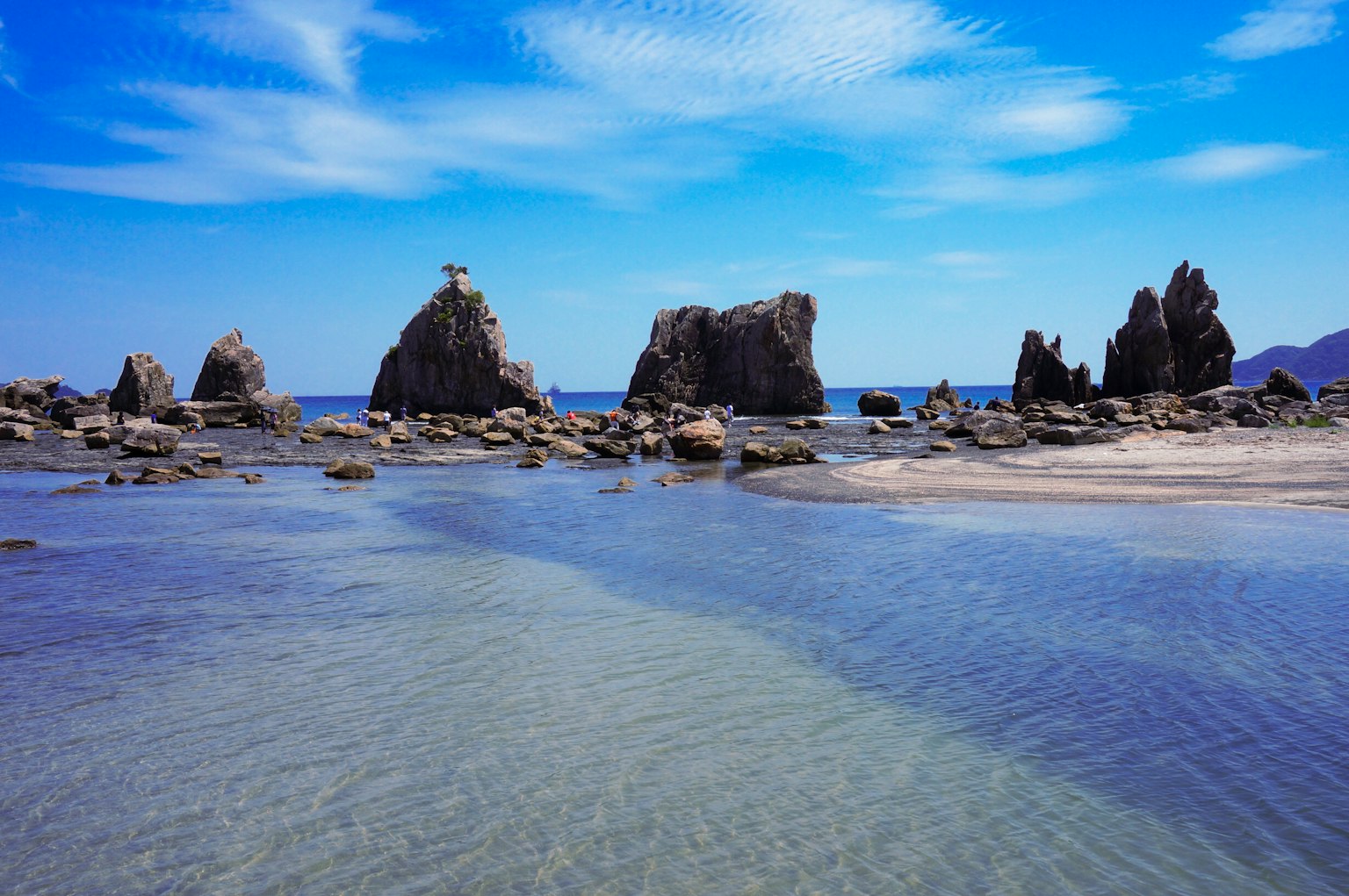 Formations rocheuses s'élevant au-dessus d'une eau claire et d'une plage de sable sous un ciel bleu