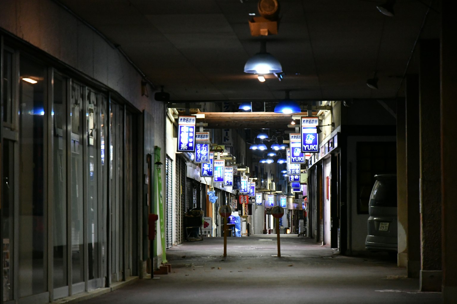 Koridor redup dengan lampu biru dan toko