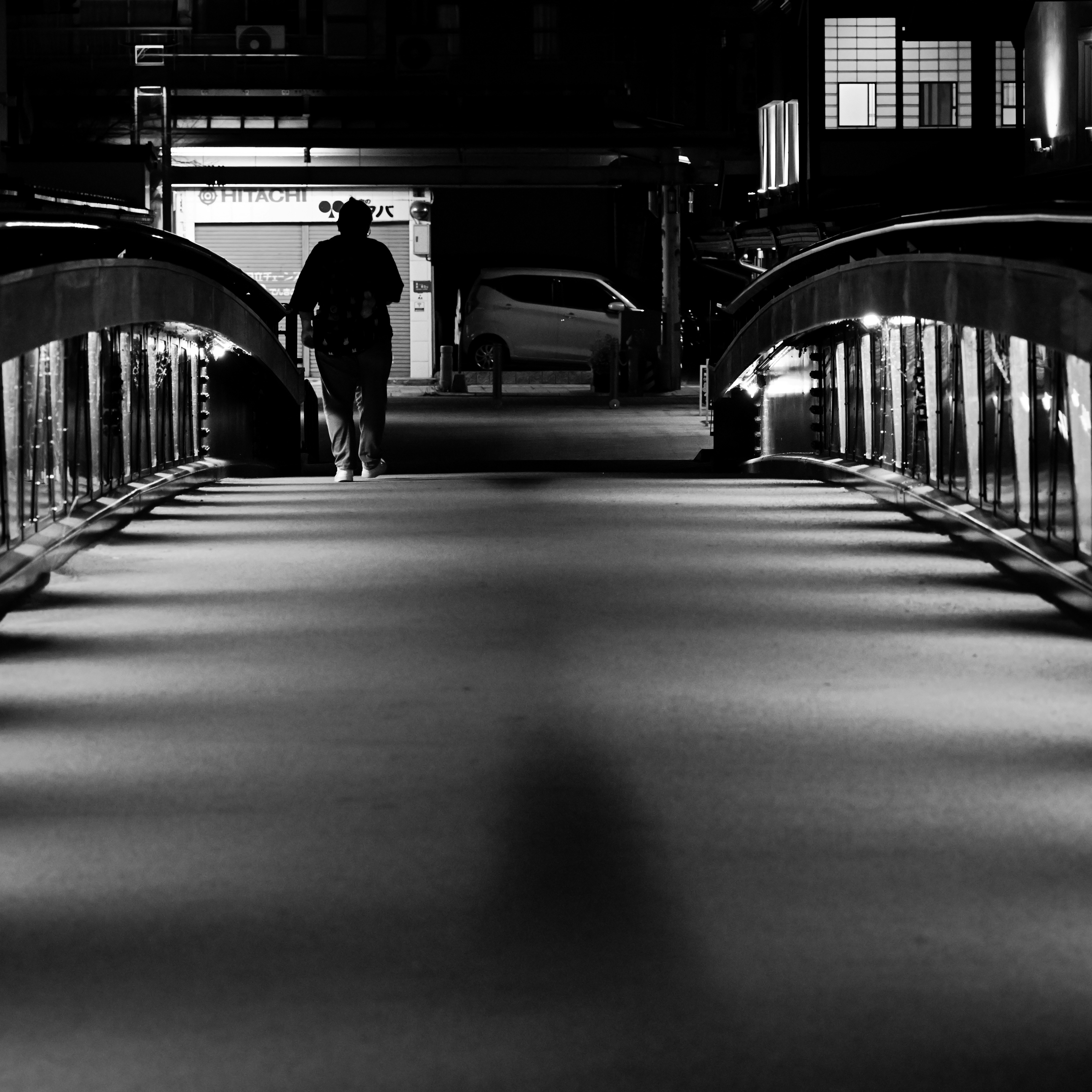 夜の橋の上で後ろ姿の人物が歩くモノクロのシルエット