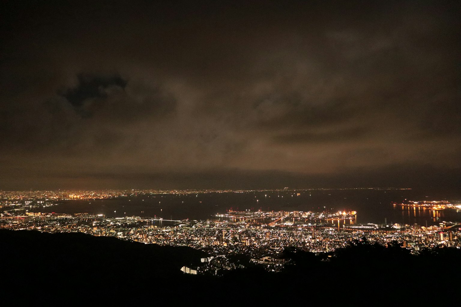 Vista panorámica de una ciudad de noche con luces iluminadas y cielo nublado