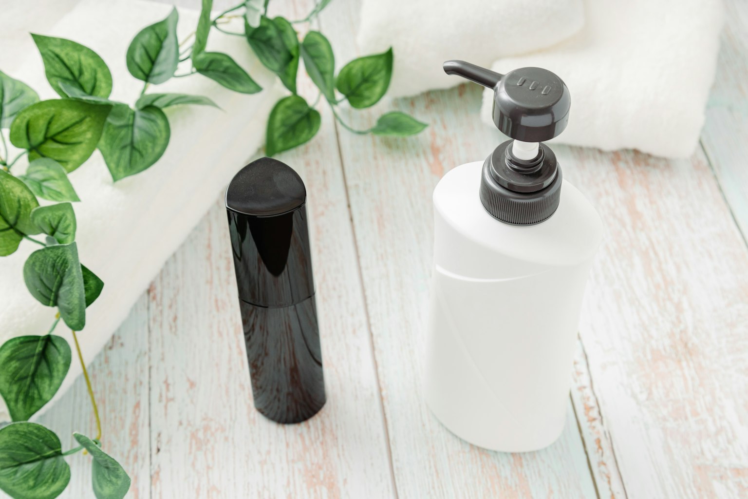 Botol hitam dan botol pompa putih di atas handuk putih dengan daun hijau