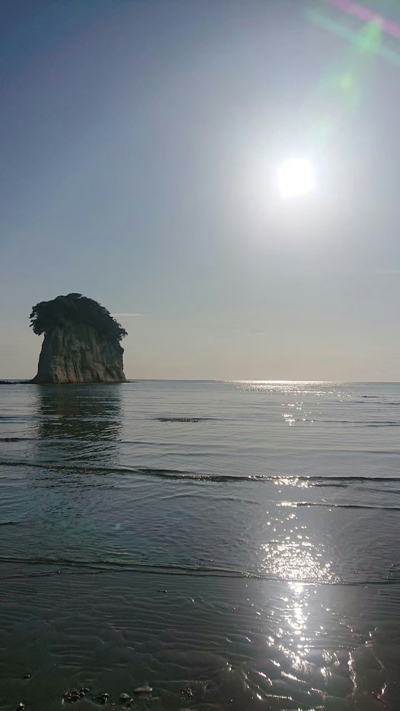 Rock formation silhouetted against the sun over the ocean