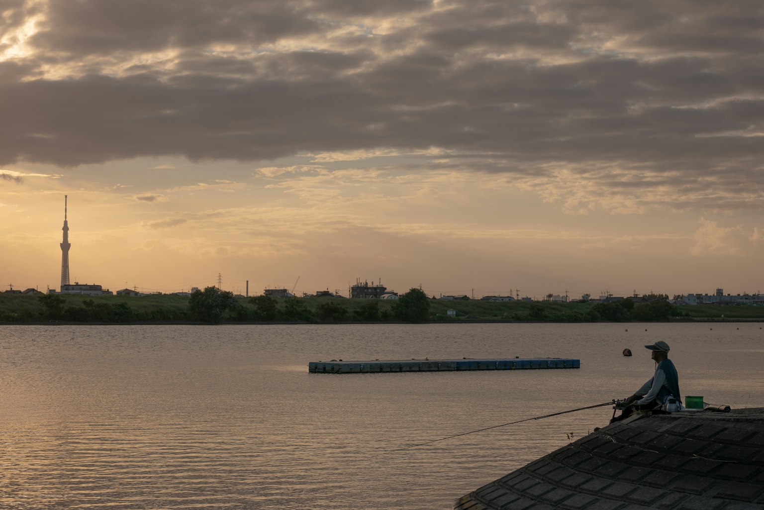 A man fishing by the river during sunset with a tower visible in the distance