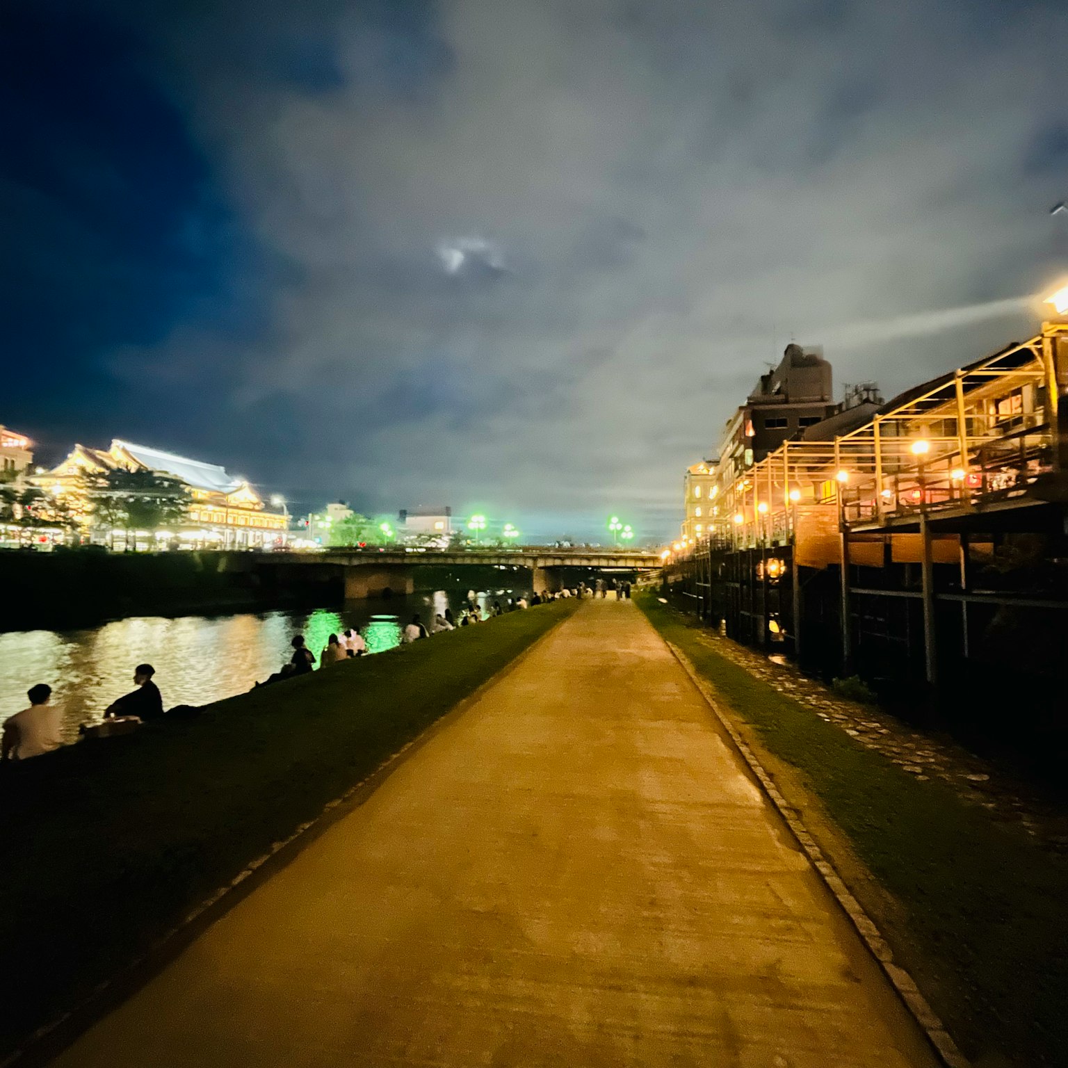 Passeggiata notturna lungo il fiume con edifici illuminati e cielo nuvoloso
