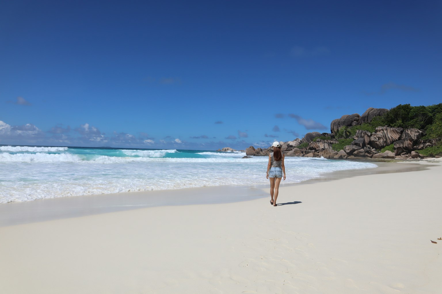 Femme marchant sur une plage de sable blanc avec océan et ciel bleus