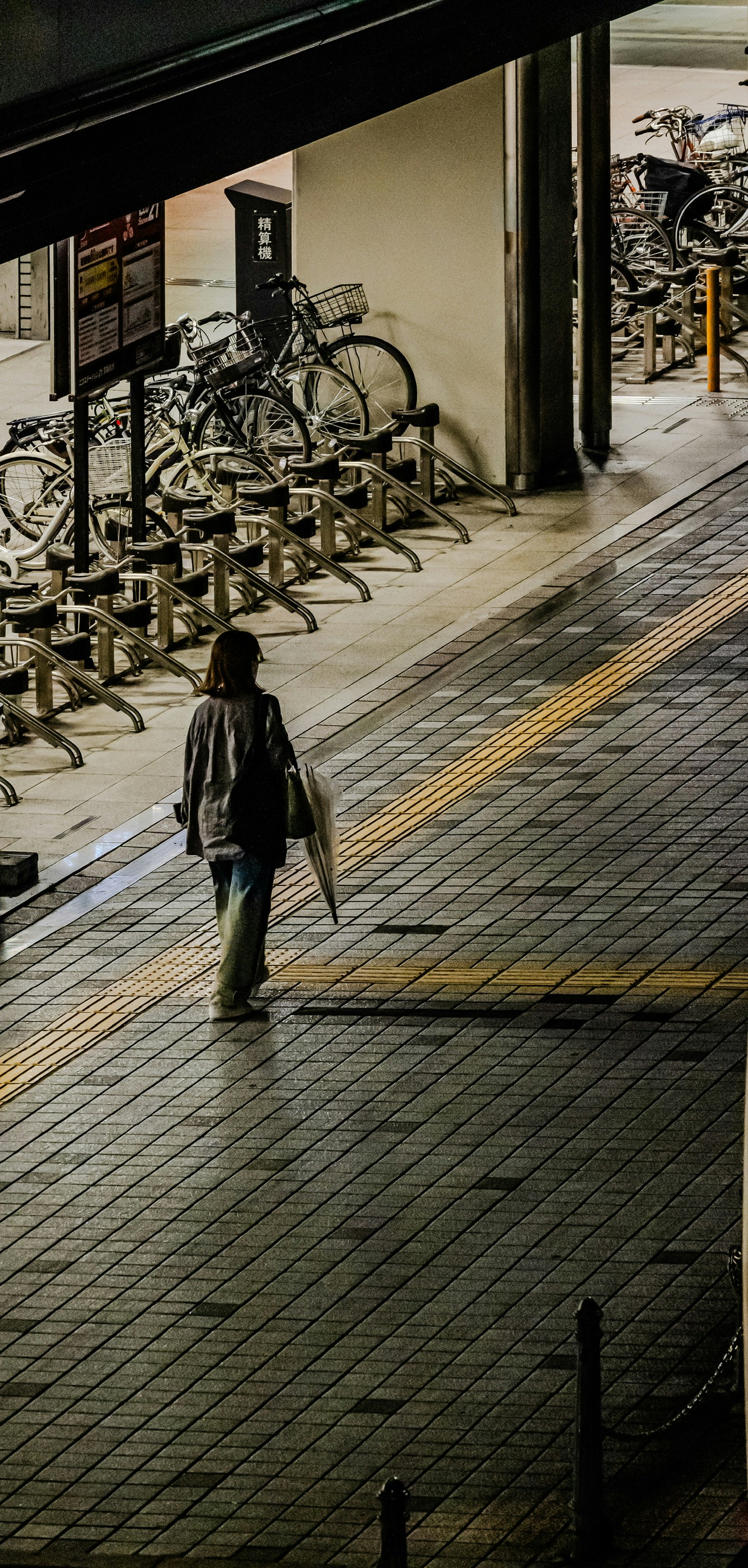 Persona che cammina con un ombrello vicino a un parcheggio per biciclette di notte