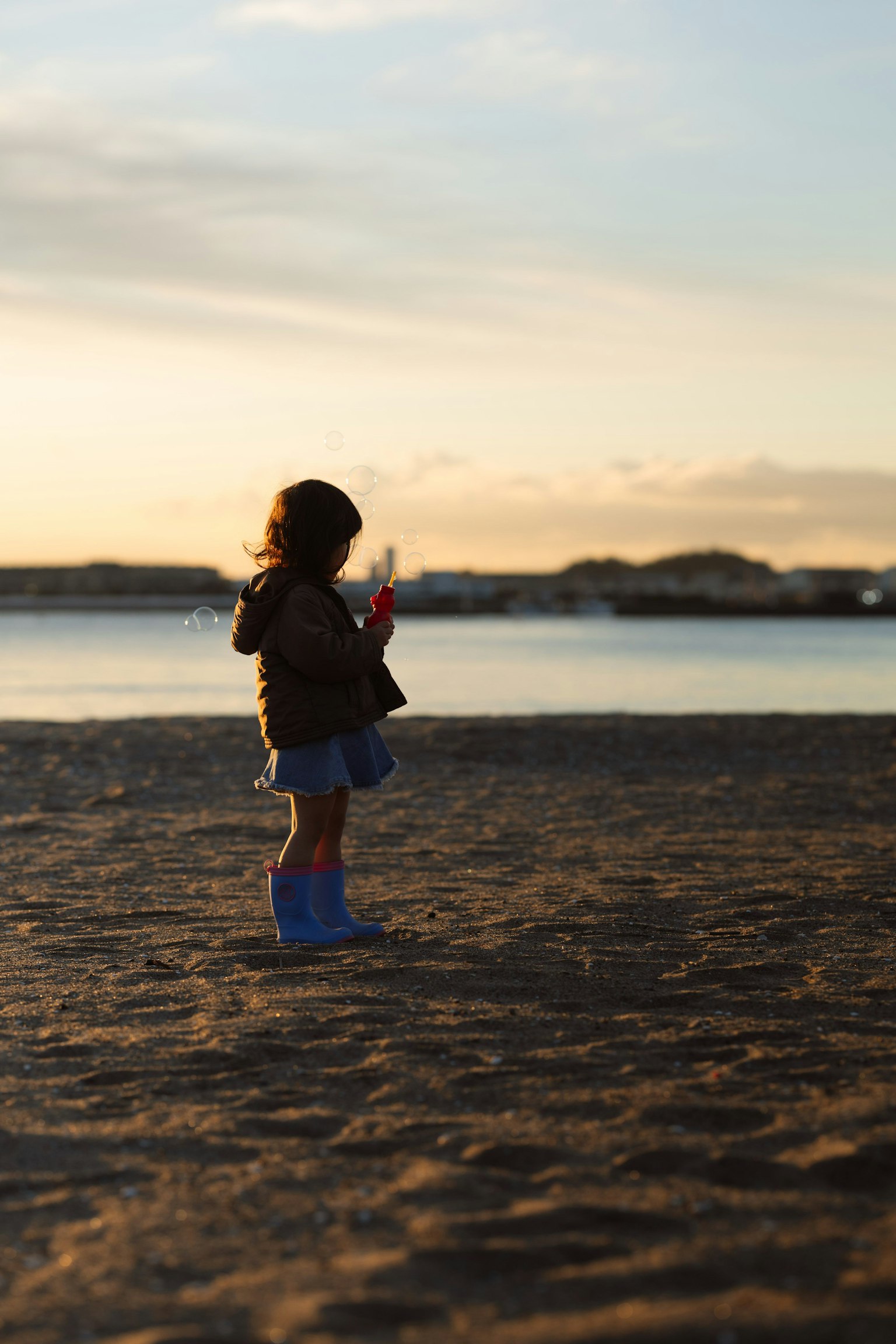 Siluet seorang anak yang berdiri di pantai saat matahari terbenam