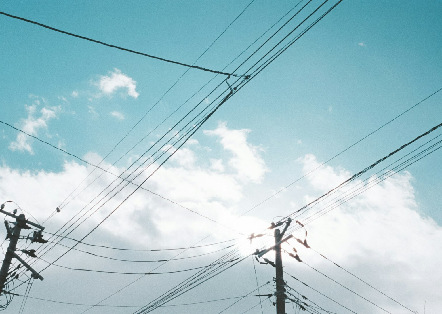 Lignes électriques croisées sous un ciel bleu avec des nuages blancs
