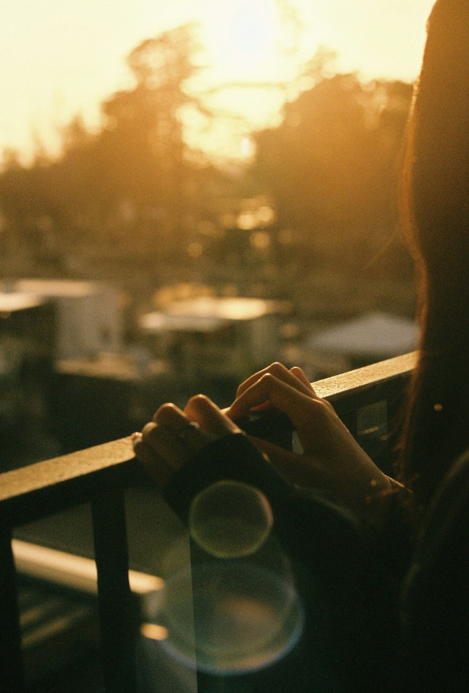 Hands resting on a balcony railing illuminated by sunset light
