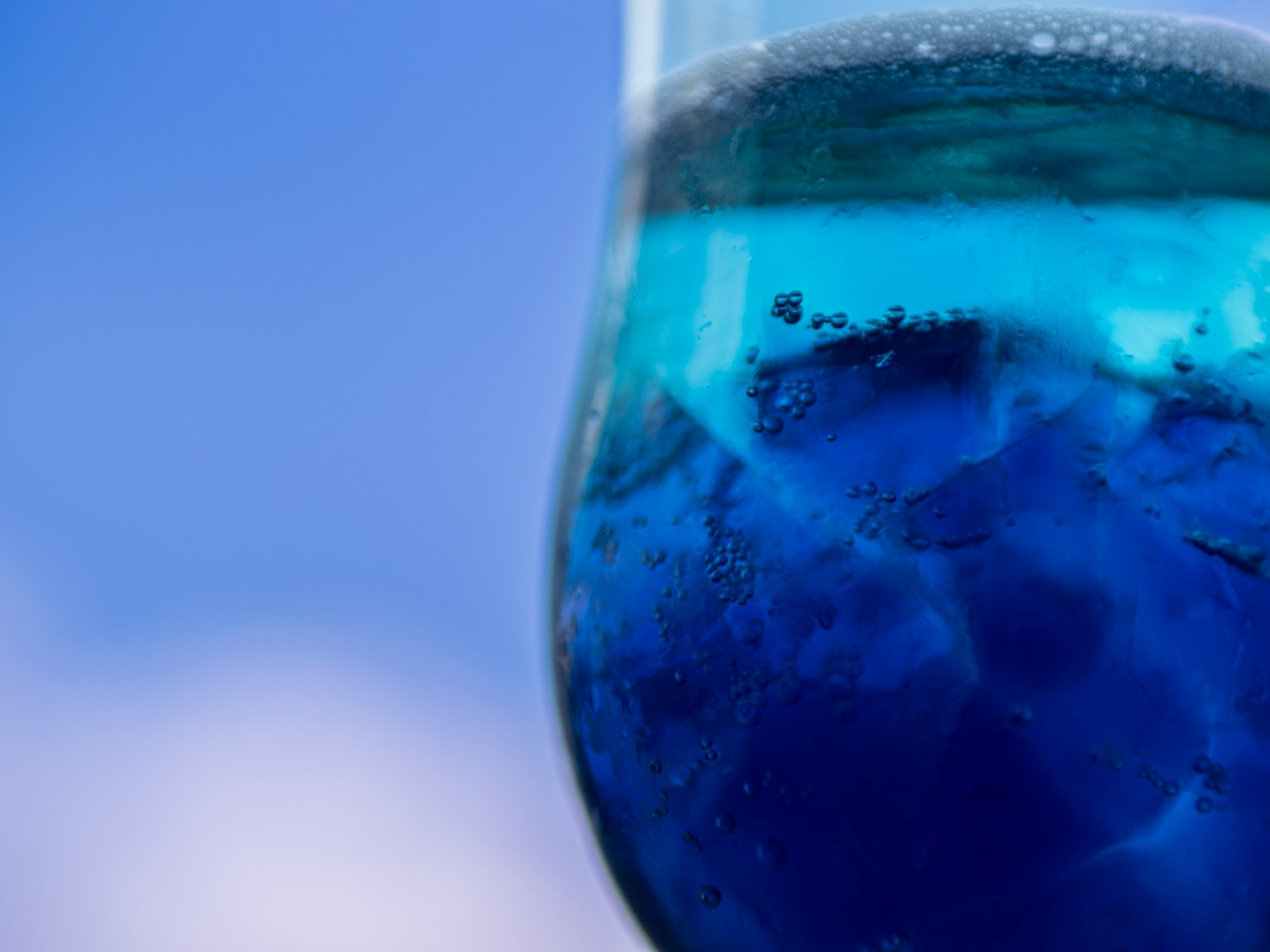 Primer plano de un vaso con líquido azul contra un fondo de cielo azul