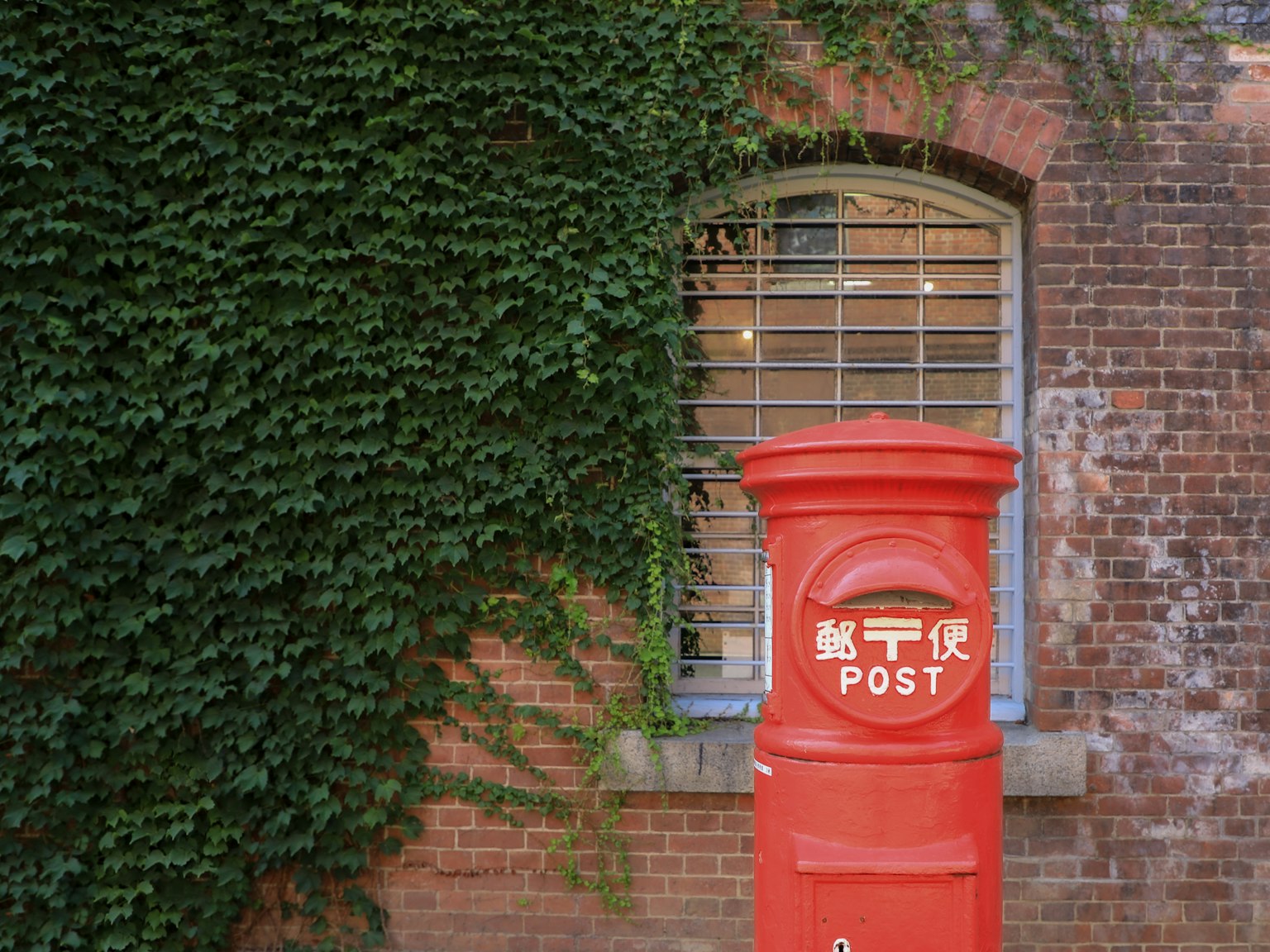 Cassetta postale rossa con edera verde su un muro di mattoni