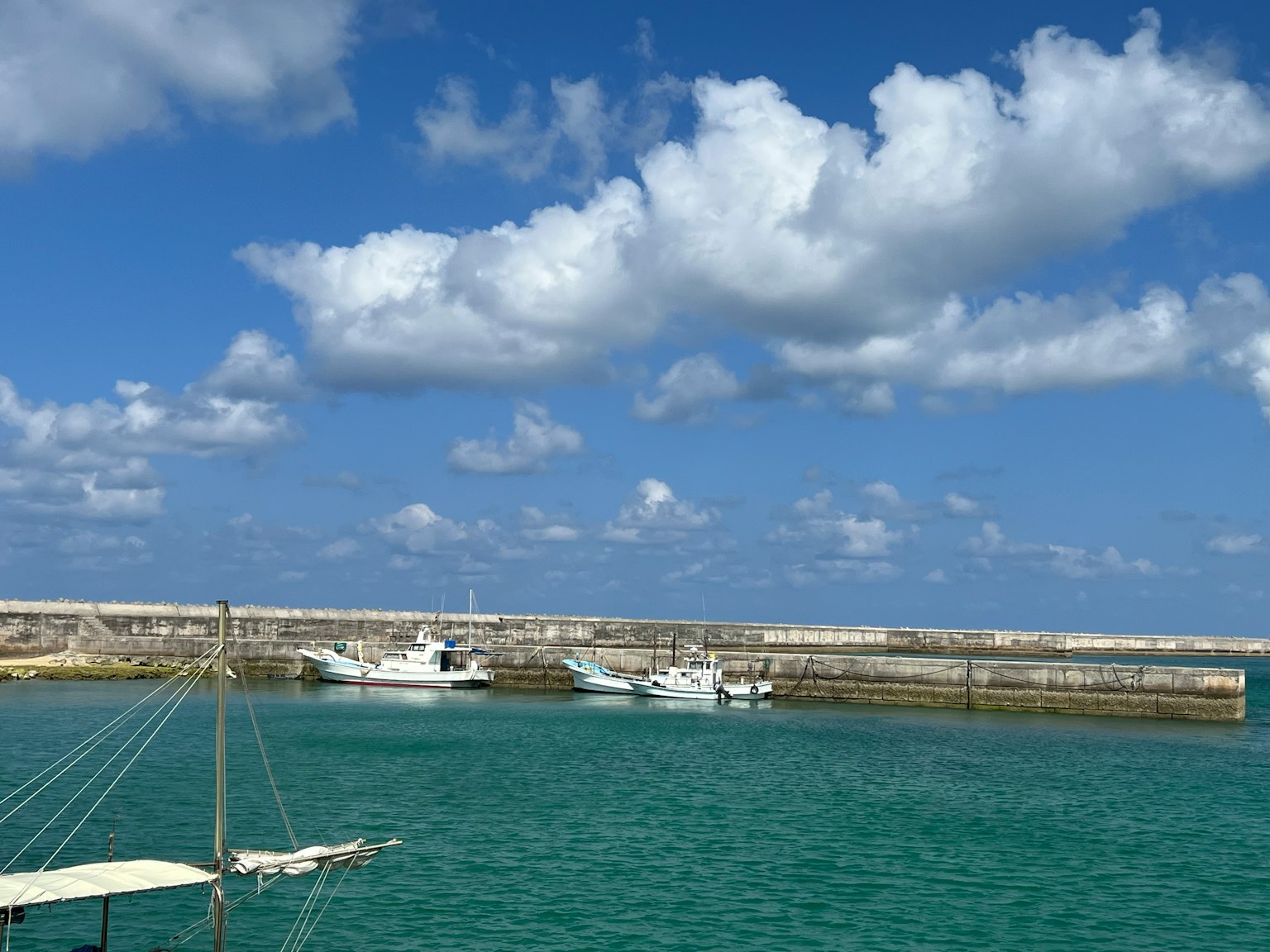 Pemandangan pelabuhan dengan air biru kehijauan dan awan putih kapal berlabuh