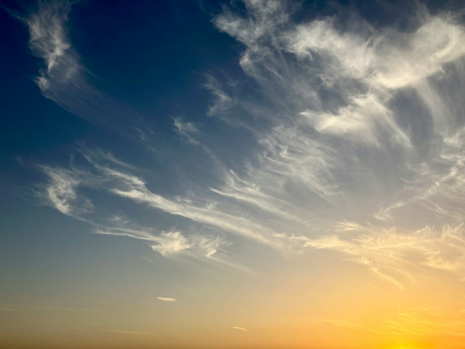 A scenic view of blue sky with wispy clouds and sunlight from the horizon