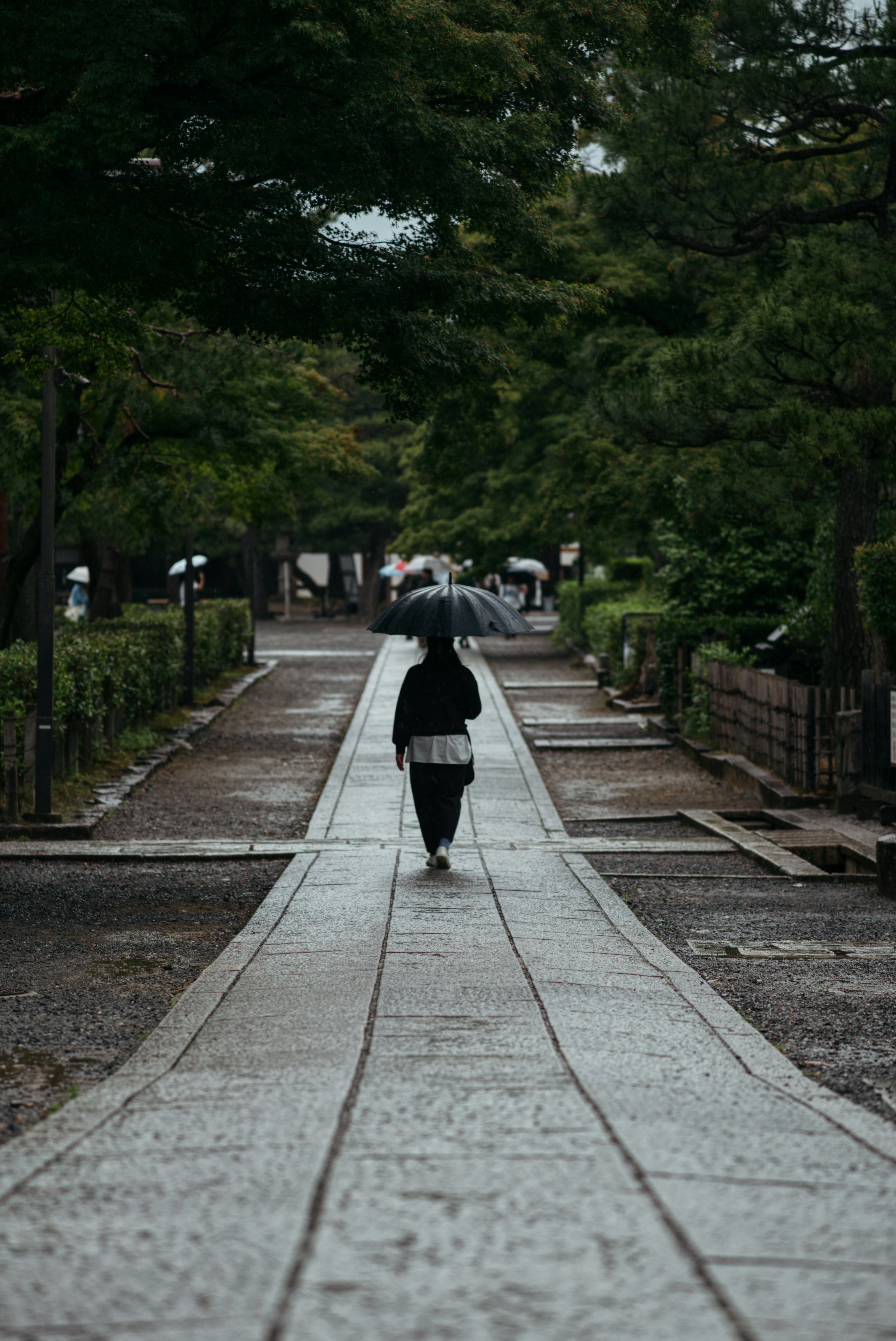 jalan batu basah di akses Kennin-ji saat hujan, dengan sosok berjalan menjauh