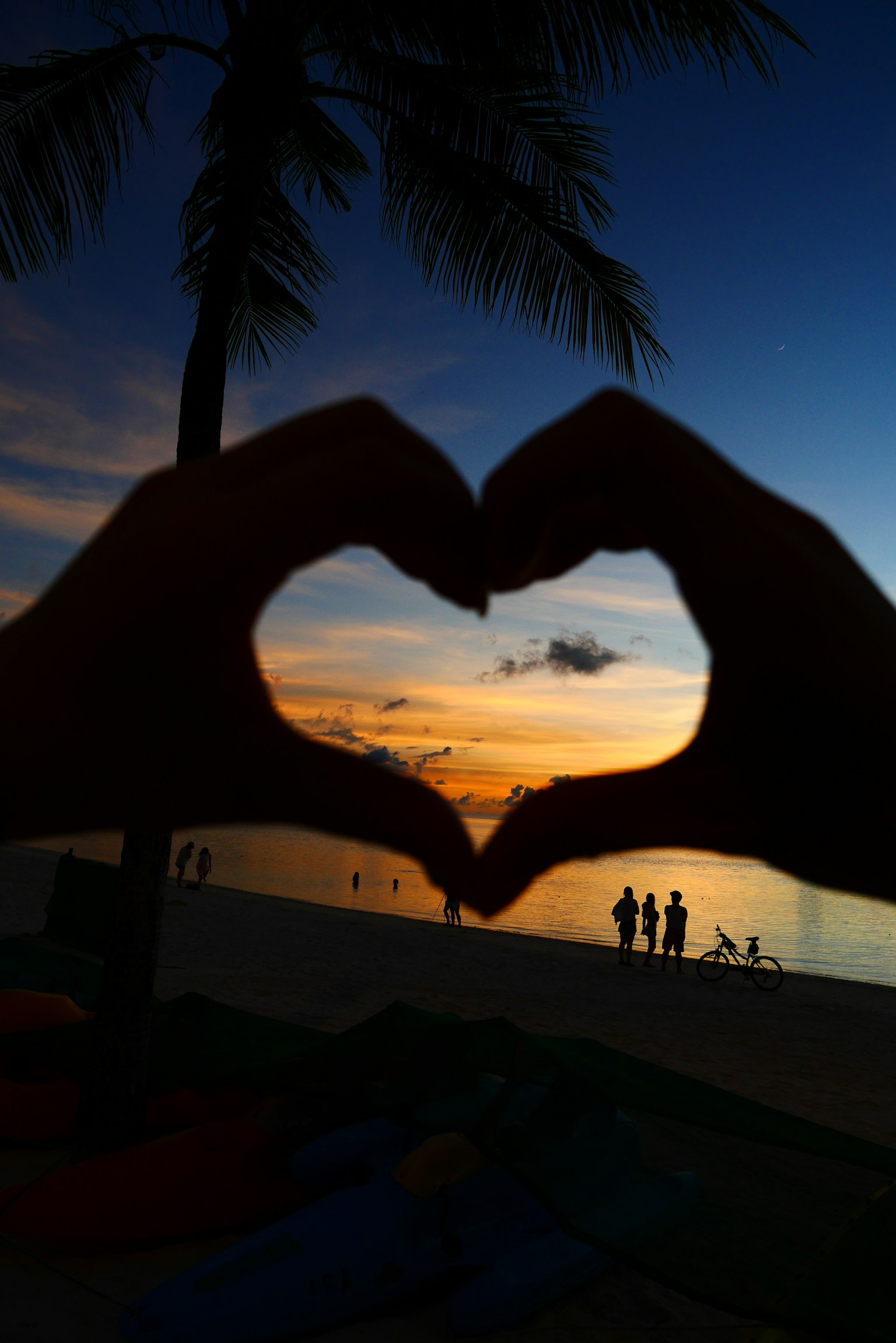Silhouette di mani che formano un cuore contro un tramonto