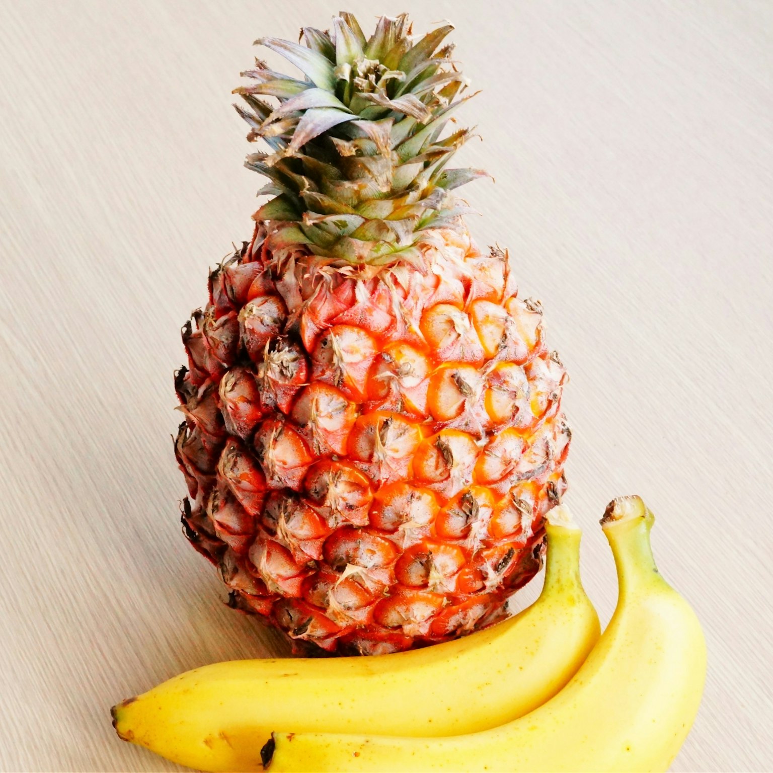 Ananas con due banane su una superficie in legno chiaro