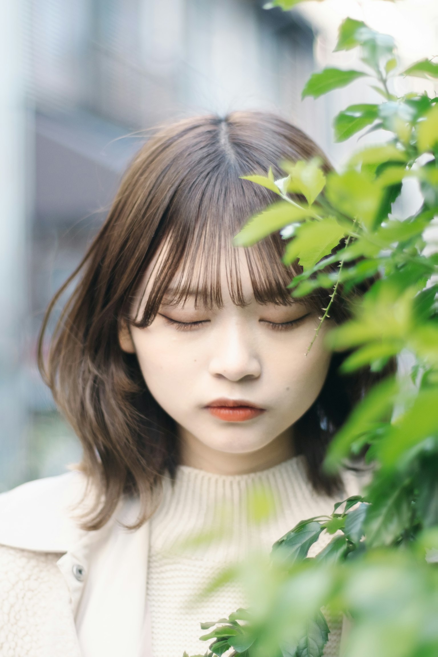 Une jeune femme se tenant parmi des feuilles vertes les yeux fermés