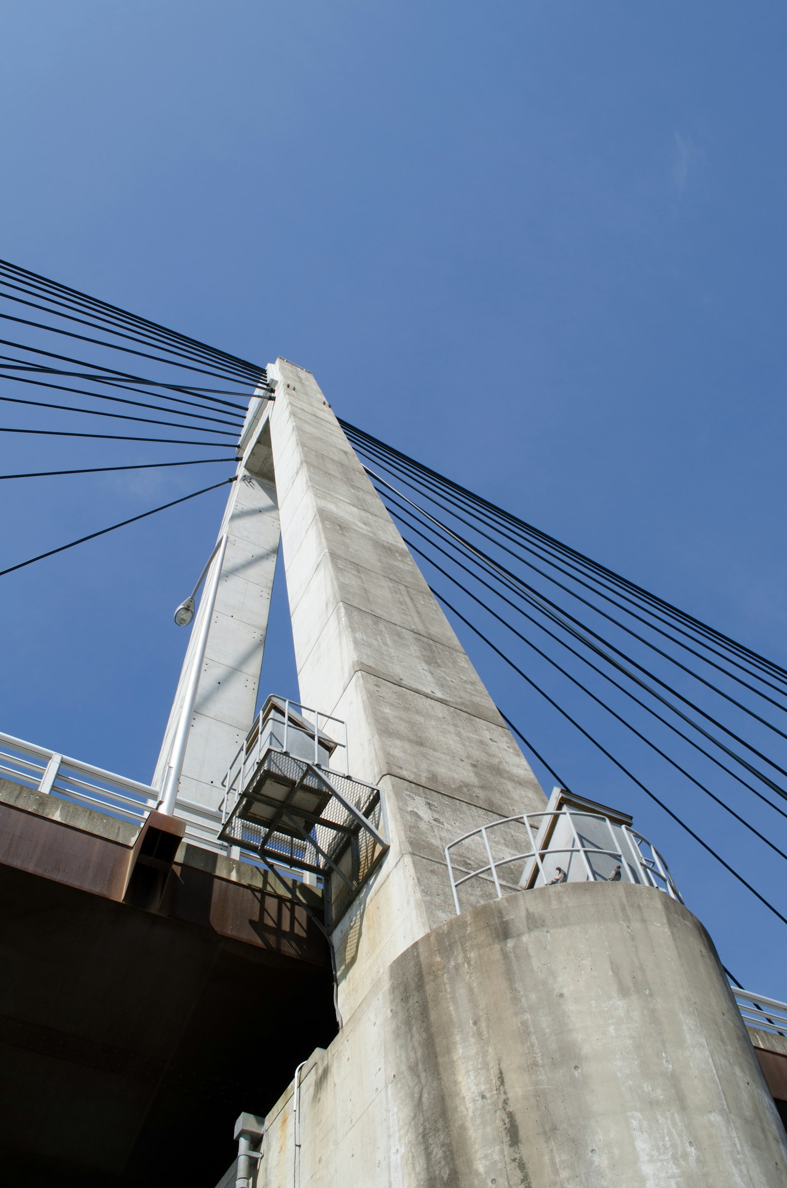 Foto melihat ke atas ke pylon jembatan tinggi di latar belakang langit biru