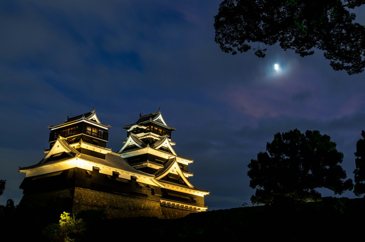 ทิวทัศน์สวยงามของปราสาทคุมาโมโตะในตอนกลางคืนภายใต้แสงจันทร์