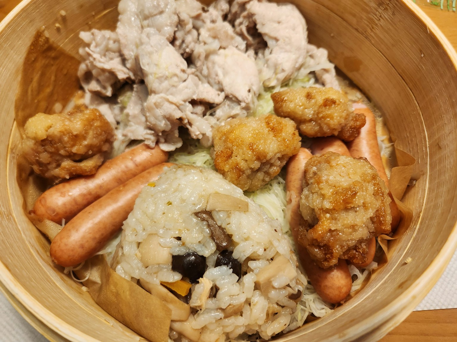 Steamed dish in bamboo container featuring pork, fried chicken, sausages, and mushroom rice