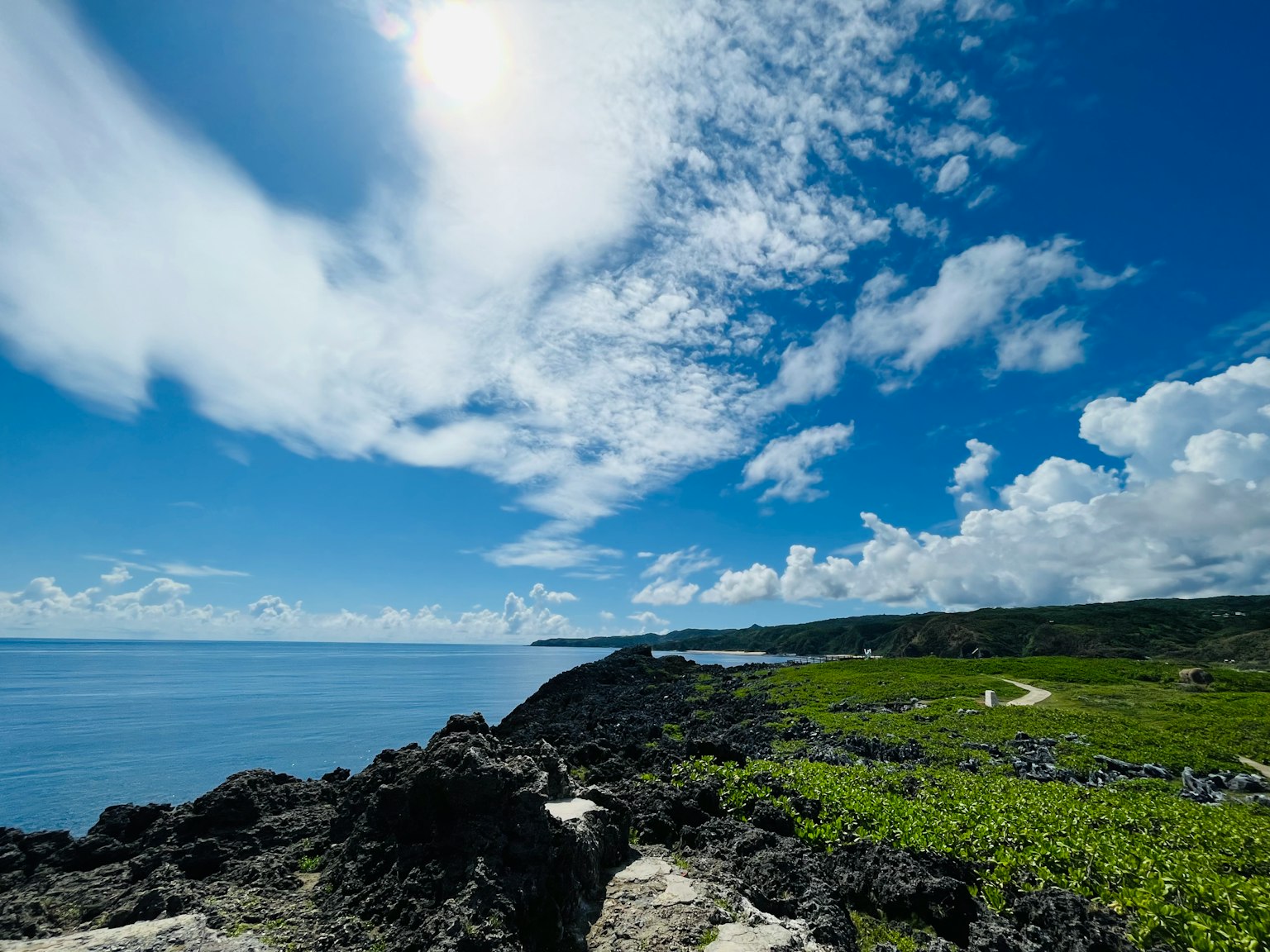 Küstenlandschaft mit blauem Himmel und weißen Wolken mit Felsen und grüner Vegetation