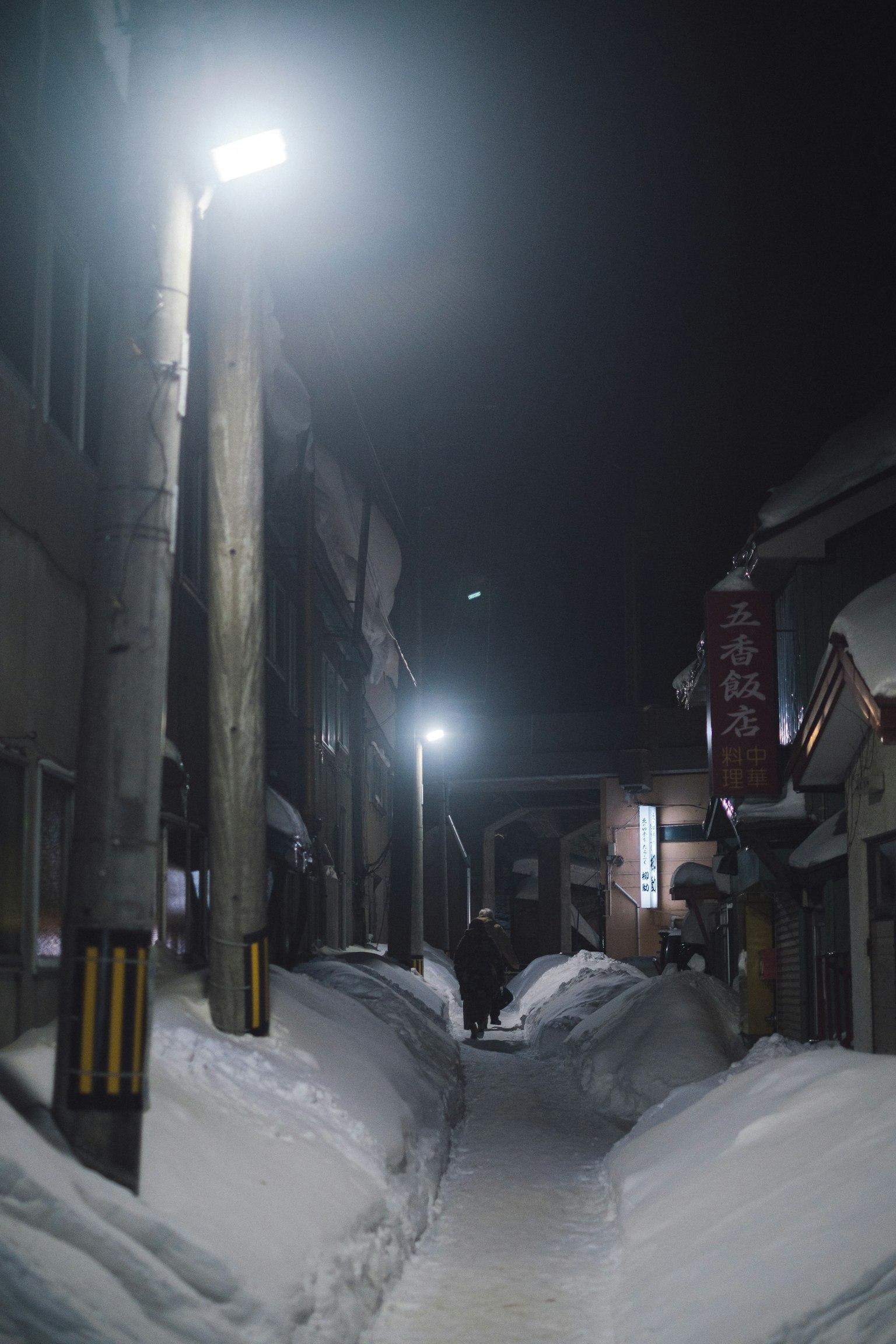 Snow-covered alley at night with streetlights and buildings