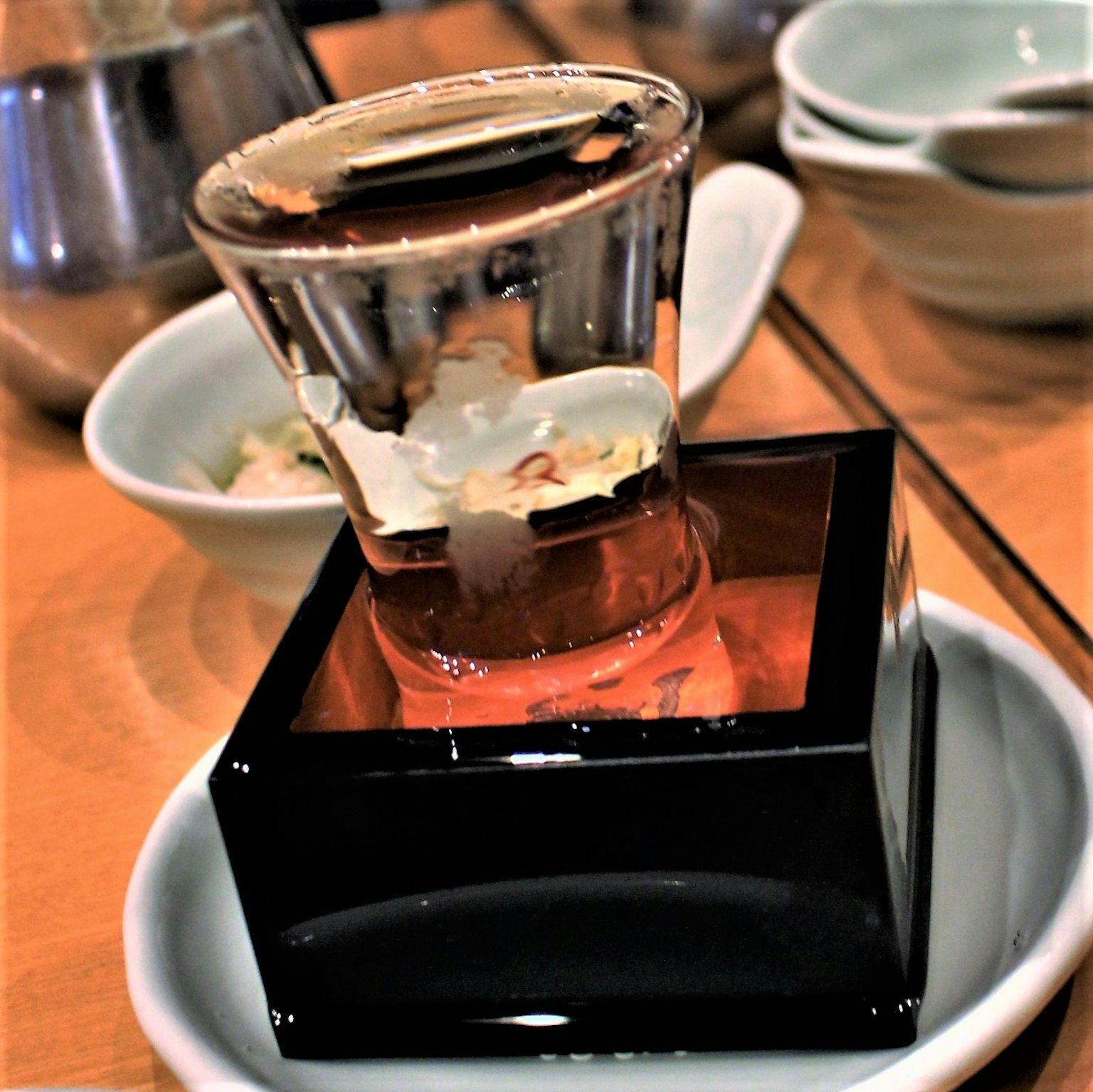 Vaso transparente de sake colocado en un recipiente cuadrado negro